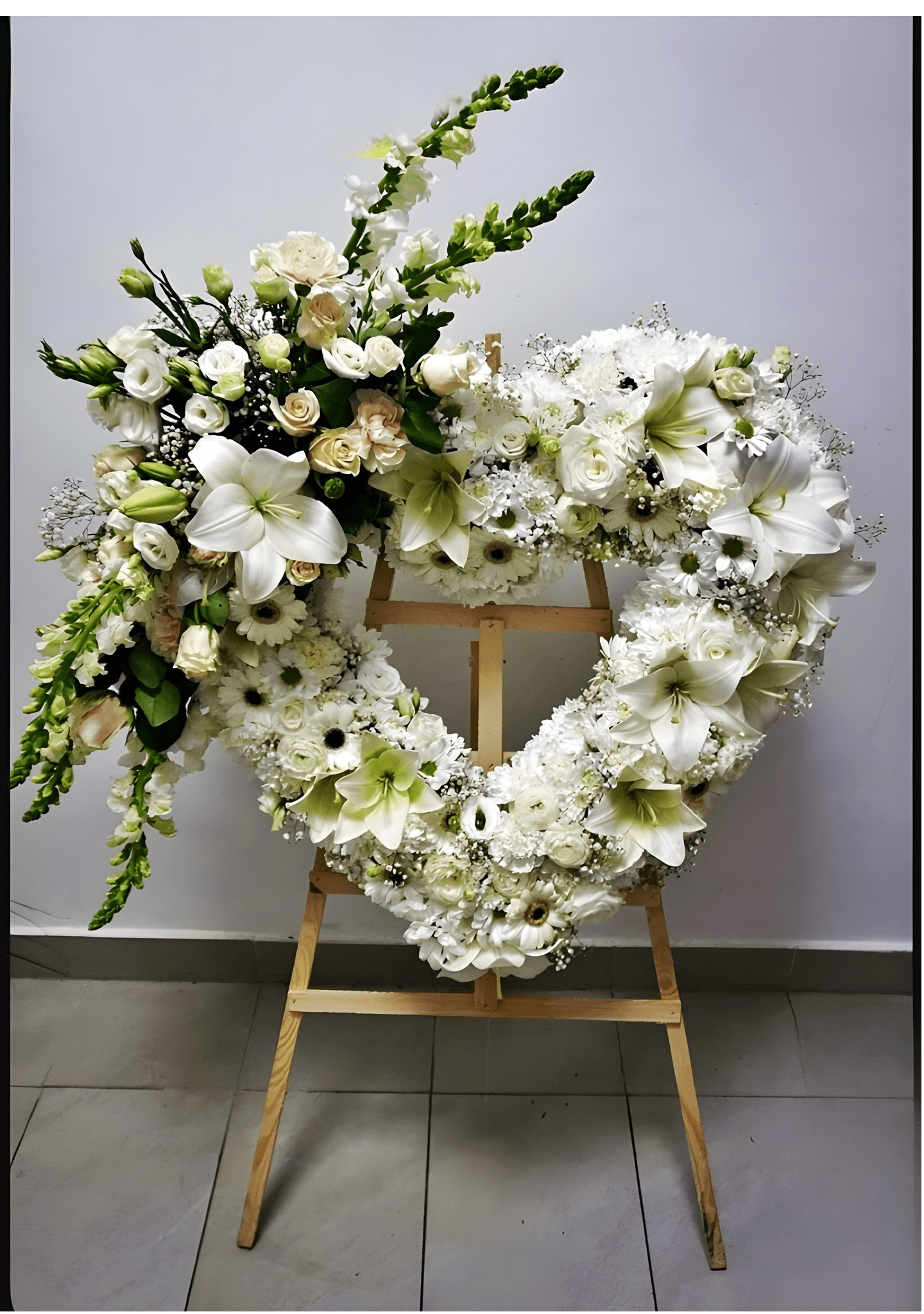 Heart of Remembrance  - A heartfelt expression of love and remembrance, this heart-shaped easel arrangement honors a cherished life with grace and beauty. Soft white daisies, lilies, roses, carnations, and snapdragons are carefully arranged to form a pure, comforting tribute. The delicate blend of flowers symbolizes peace, love, and cherished memories, while the heart shape speaks to the everlasting impact of a loved one's spirit. Perfect for honoring their memory, this arrangement brings a touch of serenity and heartfelt sentiment to the service.