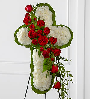 The Floral Cross Easel - The Floral Cross Easel is a symbol of love and faith to honor the deceased at the final farewell service. White carnations are arranged to form a cross in which an accent of red roses, spray roses, and lush greens are draped across the center, creating a beautiful display of serene elegance. Displayed on a wire easel.