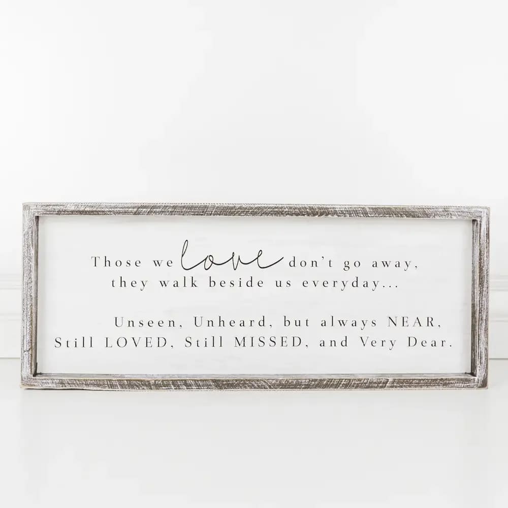 Those We Love Wood Sign - This elegant memorial sign is a heartfelt tribute to cherished loved ones who have passed away. Featuring a classic design with a white background and black lettering, it conveys the comforting message: &quot;Those We Love Don't Go Away, They Walk Beside Us Everyday... Unseen, Unheard, But Always Near, Still Loved, Still Missed, And Very Dear.&quot; With dimensions of 22&quot; by 9&quot; by 1.5&quot;, this versatile piece can be hung on a wall or displayed on a table. It's a meaningful way to express love and remembrance for departed family members, friends, or pets. Note: Standard size includes sign only. Deluxe and Premium sizes include the sign in a floral arrangement with colors and blooms appropriate for the season.