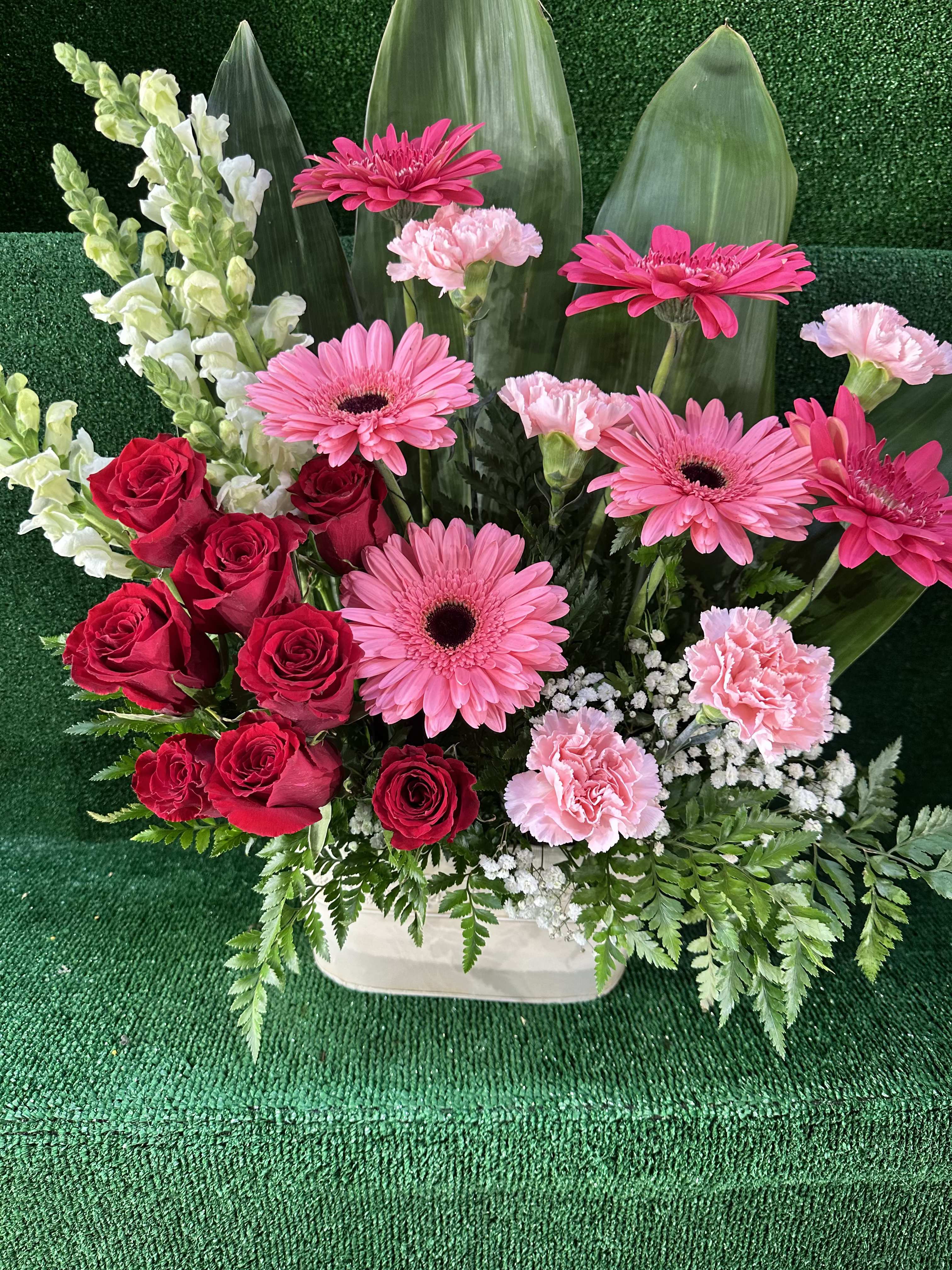 Mixed Roses, Snapdragons, Gerbera Daisies &amp; Carnations Arrangement - Brighten any occasion with our vibrant Mixed Roses, Snapdragons, Gerbera Daisies &amp; Carnations Arrangement. This stunning display combines the timeless elegance of roses, the playful charm of Gerbera daisies, the delicate beauty of snapdragons, and the soft, classic touch of carnations.  Expertly arranged with lush greenery, this bouquet is perfect for birthdays, anniversaries, or simply to add a splash of color and joy to someone’s day.