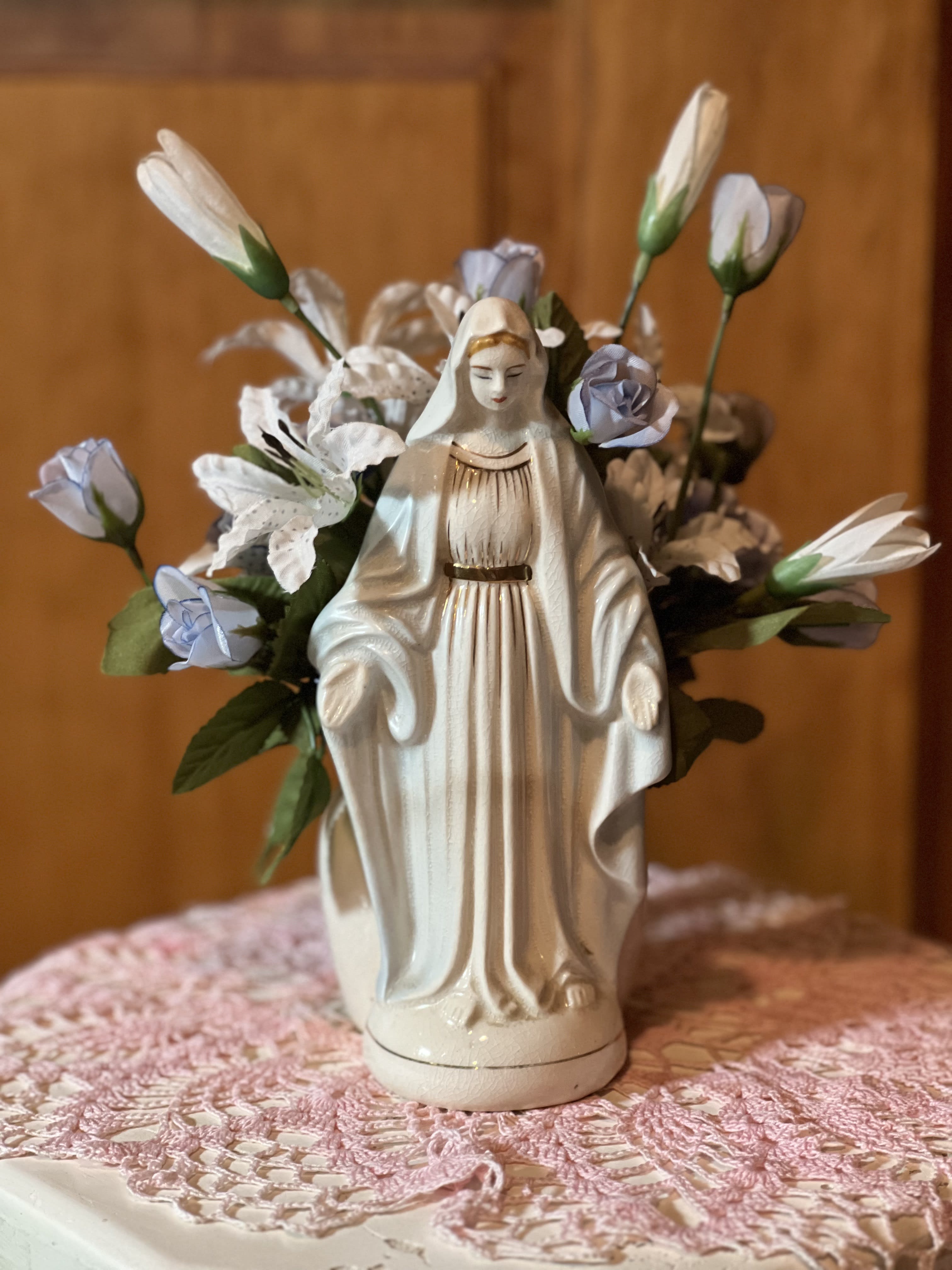 Mother Mary with Silk Flowers Mother Mary with Silk Flowers - Mother Mary with silk flowers. Approximately 7" tall. Porcelain figurine of Mother Mary with out stretched arms. Accented with gold paint. Vintage piece. Perfect for your home decor area.