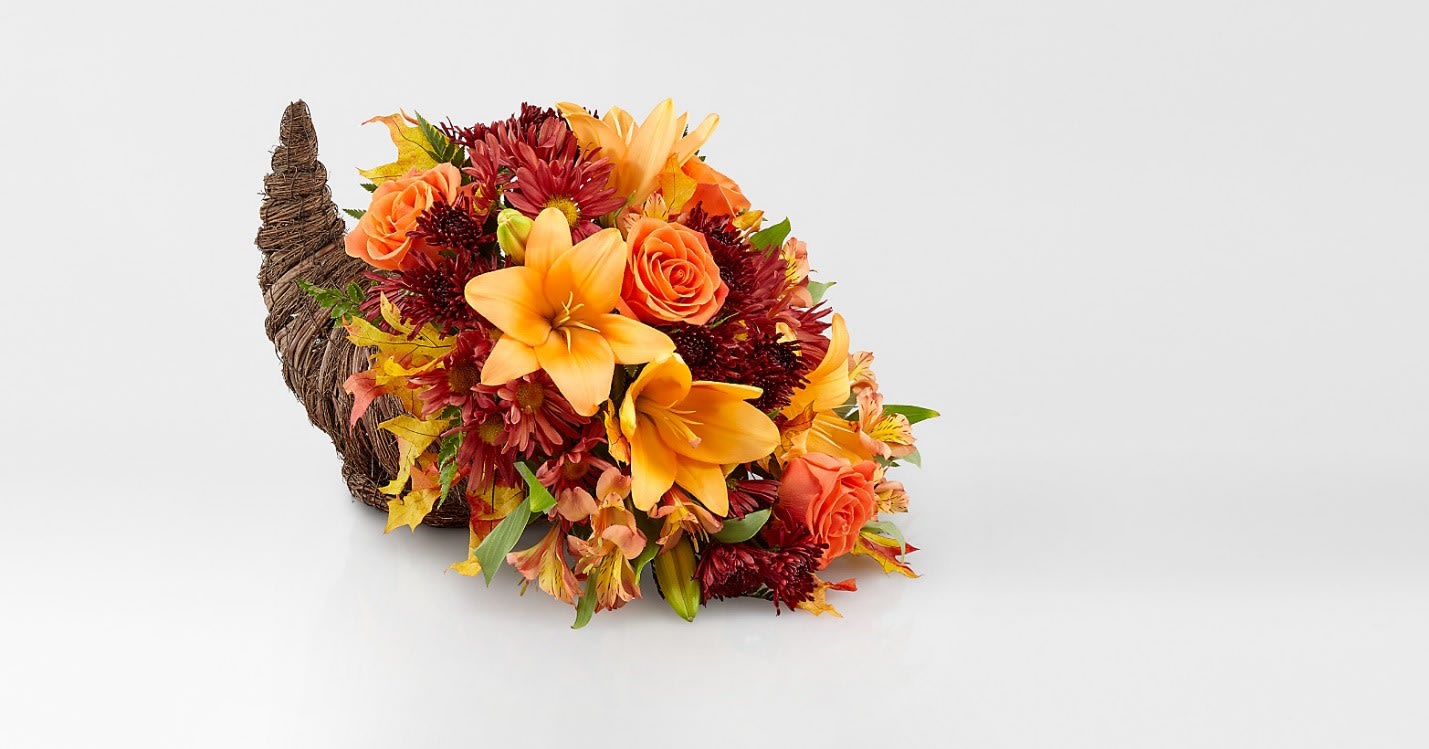 HARVEST CORNUCOPIA HARVEST CORNUCOPIA - "SET: One-Sided Celebrate the season of Thanksgiving with this traditional symbol of autumnal abundance. The perfect Thanksgiving table decoration, this beautiful cornucopia is rendered as a horn-shaped wicker basket filled with fall flowers and harvest wheat. Also, ideal for the kitchen counter, coffee table or entryway. Gorgeous sunflowers and lush orange roses are accented with unique blue eryngium, red daisies, yellow cushion mums, parvifolia eucalyptus and magnolia leaves in a wicker cornucopia-shaped basket. Cinnamon sticks and harvest wheat are comforting fall touches."