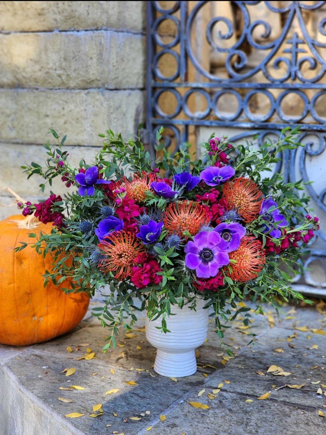 Melodic Mosaic  - This arrangement is a vibrant, modern garden-style masterpiece perfect for any special occasion. It features striking purple anemones as the centerpiece, paired beautifully with the warm, spiky textures of orange proteas.