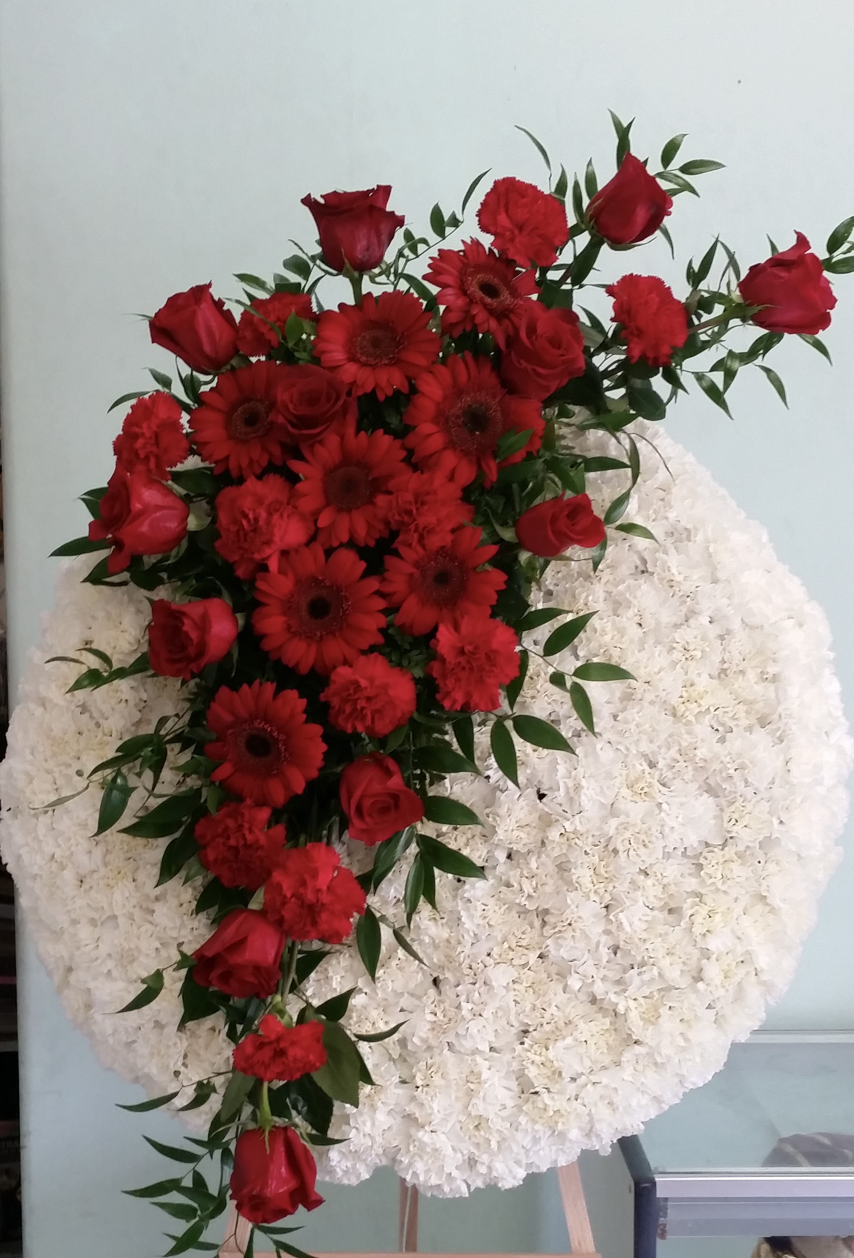 Circle of Comfort Circle of Comfort - Solid wreath with white carnations, red carnations, red roses, and red gerbera daisies.