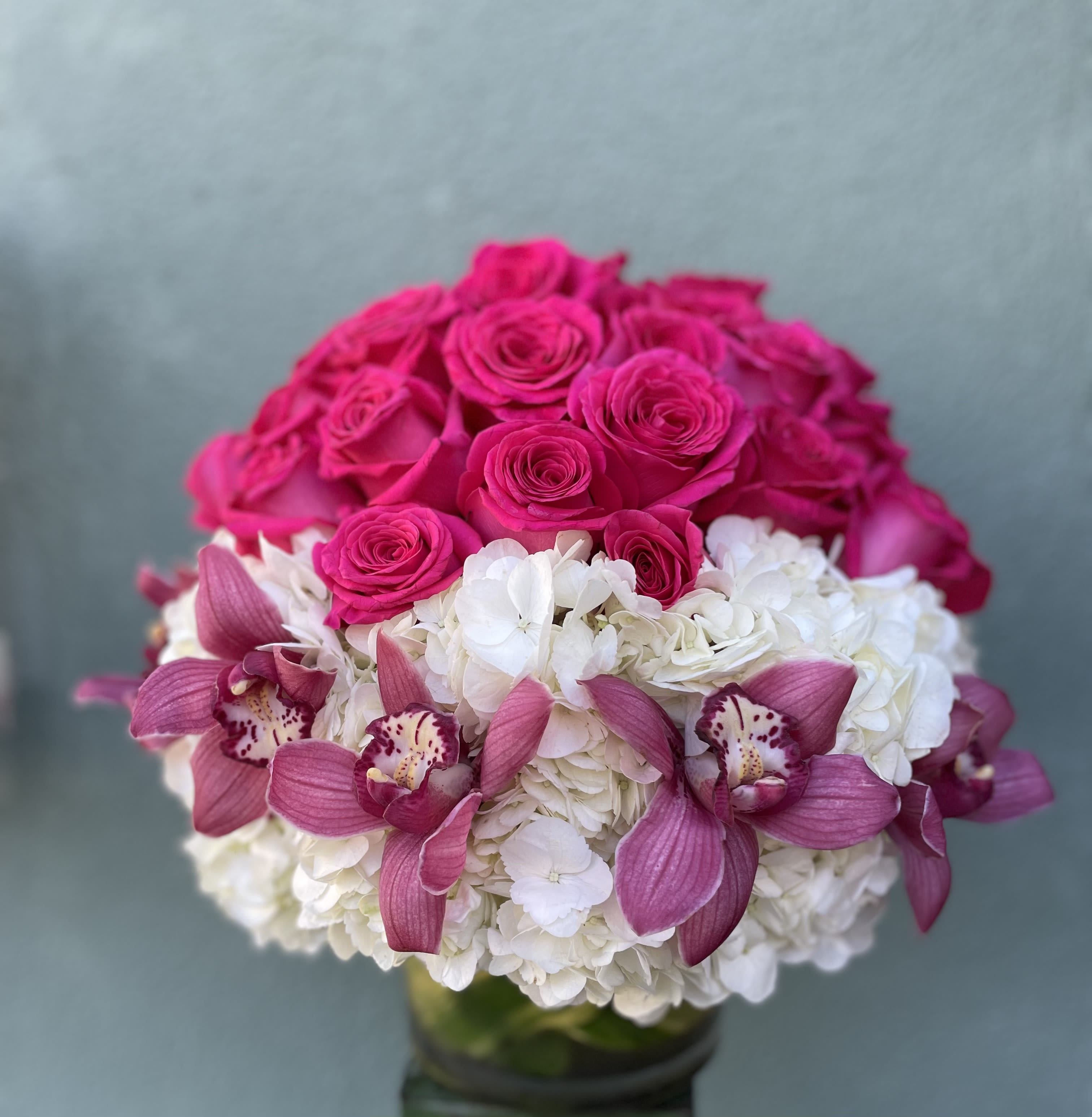 Pink Sparkle - This arrangement includes hot pink roses with cymbidium orchids all hand arranged in glass vase.