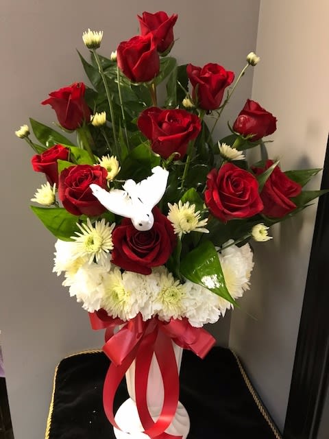 Blessed Day Blessed Day - This beautiful arrangement of a dozen Red Roses are arranged in a bed of white crysanthemums, white carnations and accented with a white dove and red bow.