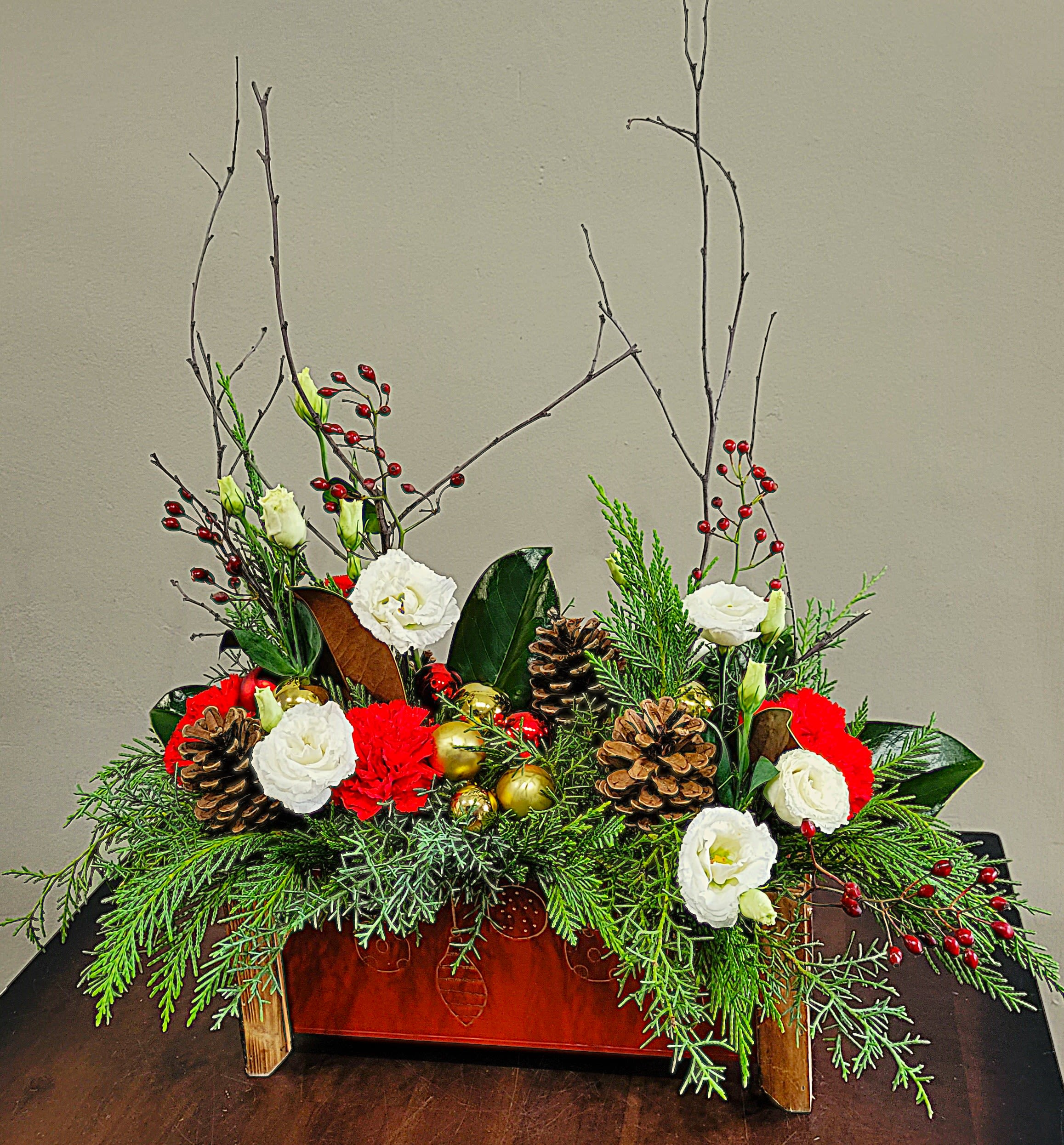 Deck the Halls  - A decorative metal and wood trough filled with a mix of winter pine evergreens, magnolia, pine cones, festive baubles, birch and red berries, Lisianthus and your choice of Carnations or upgrade with roses.   