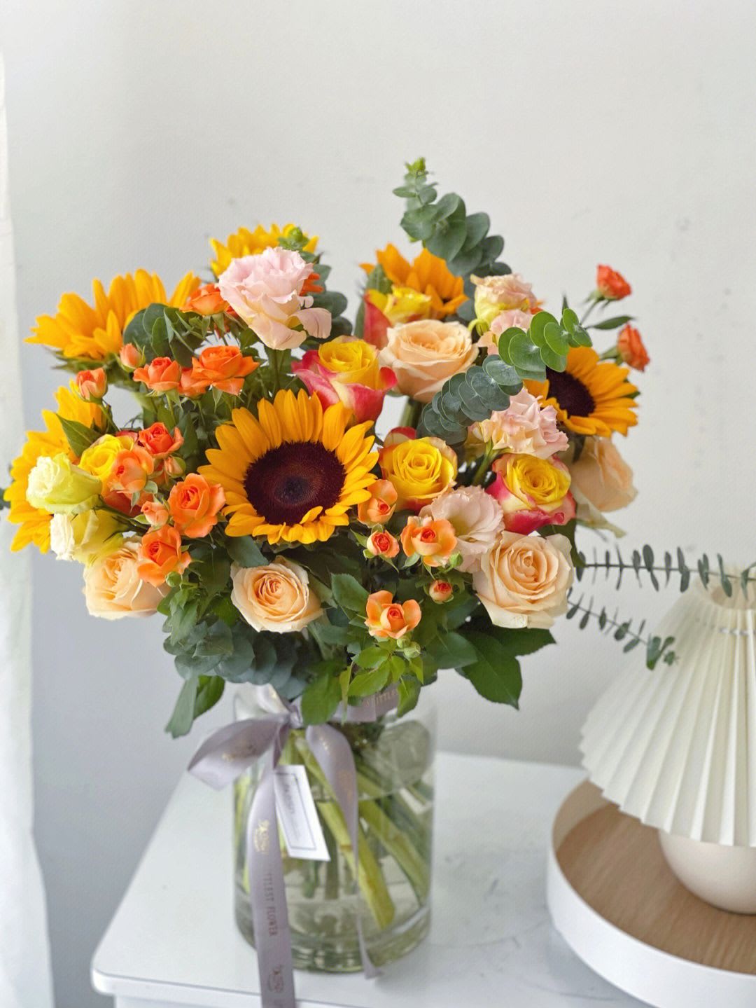 sunshine - Contains orange sunflowers, pink lisianthus, champagne roses, eucalyptus leaves, multi-headed roses, in a glass bottle transparent container