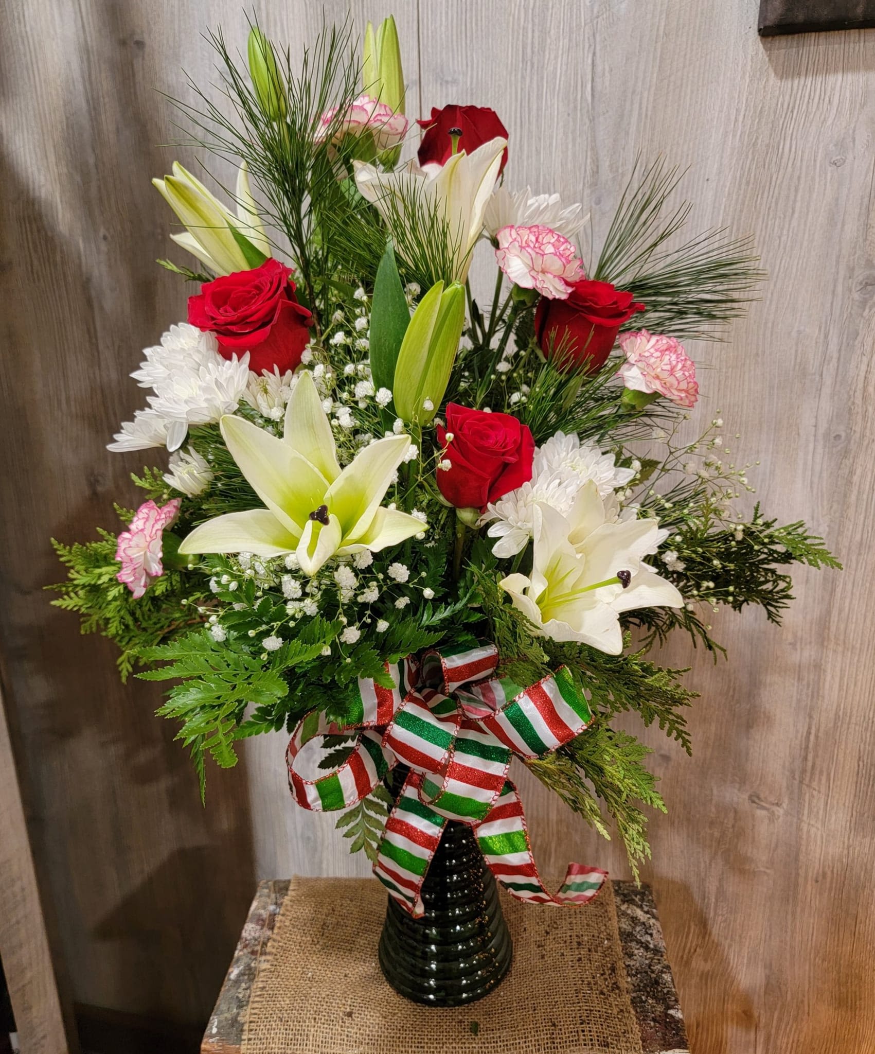 Holiday Cheer - Beautiful holiday vase arrangement with white lilies, red roses, and peppermint carnations arranged in a bed of fresh pine! Perfect way to spread holiday spirit! 