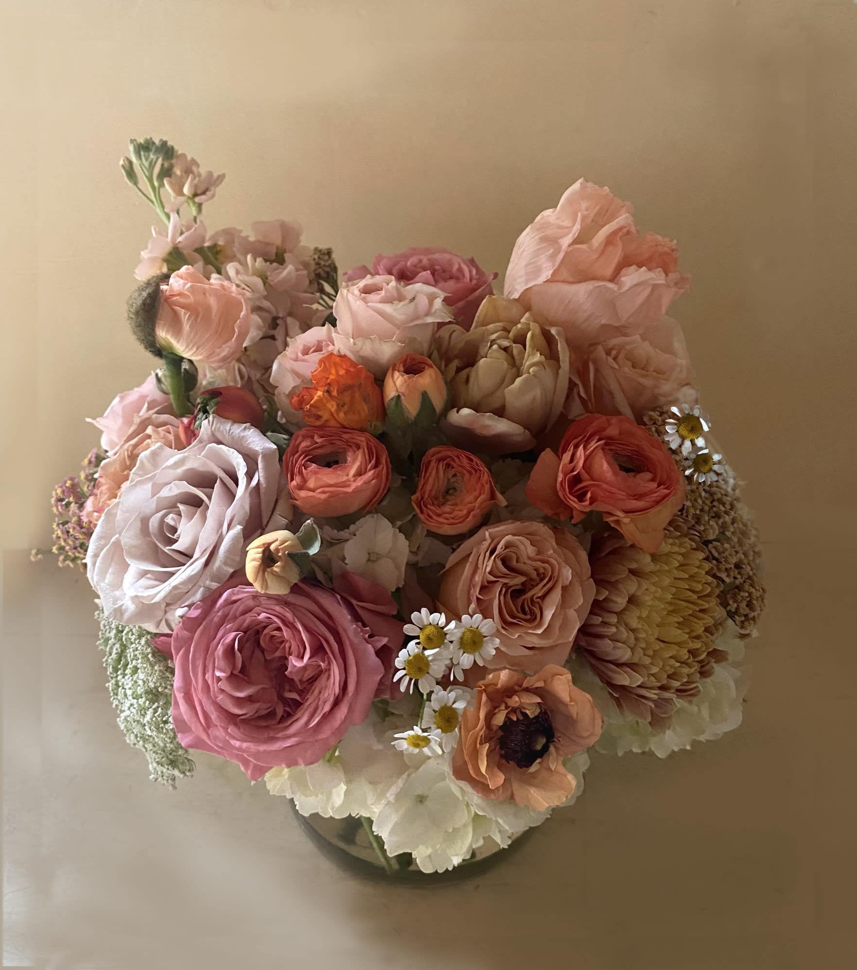 Goldie arrangement - Sunset colors of orange, brown, coral, mustard and golden pastels adorn this LA arrangement for the sweetest floral treat. Perfect for the table, the gift for the host or a gift of love for someone who needs a little cheer! Seasonal stems like poppies, roses, ranunculus, crysanthemums. Placed in a 5&quot; by 5&quot; clear vase. Go for Deluxe or Premium for bigger vase and more stems.