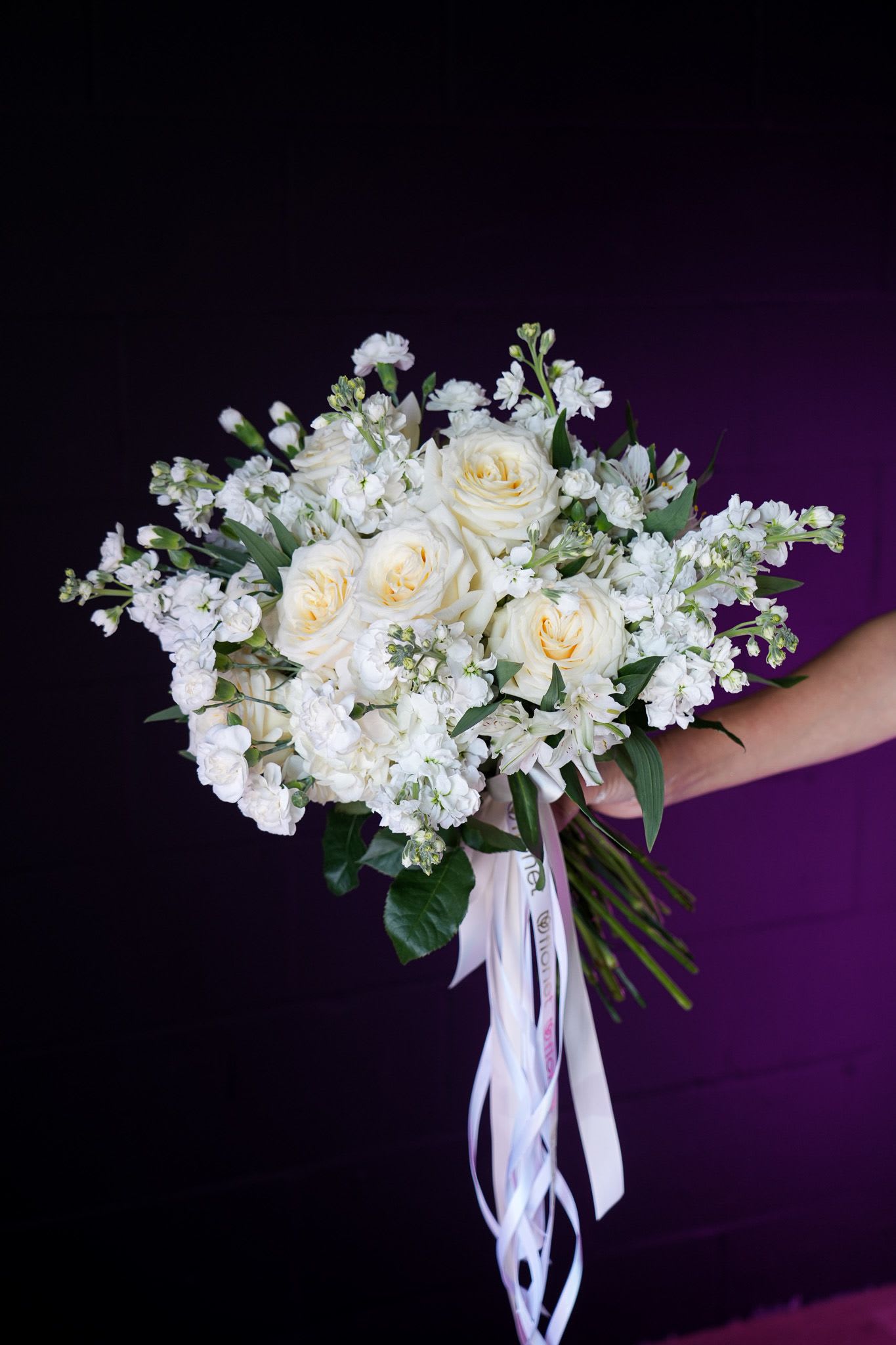Ivory Elegance Bouquet Ivory Elegance Bouquet - The Ivory Elegance Bouquet is a graceful and timeless arrangement, featuring creamy white roses paired with delicate white stock flowers and accented by lush greenery. Its soft, neutral palette makes it perfect for weddings, anniversaries, or as a heartfelt gesture of peace and love. Tied with flowing white ribbons for an added touch of sophistication, this bouquet exudes pure refinement and charm, making it an exquisite gift for any occasion.