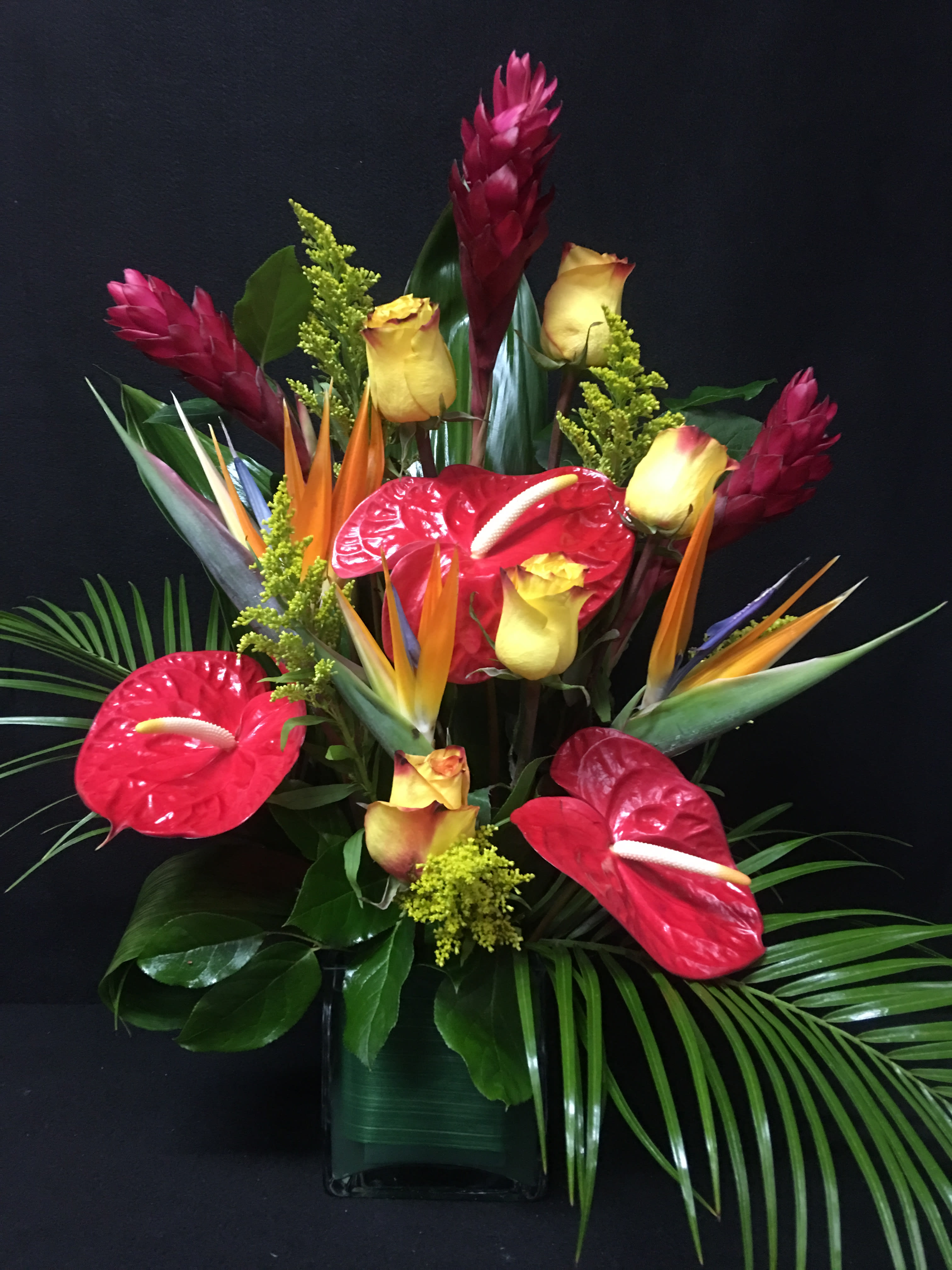 Tropical Paradise - This truly original, hand-designed arrangement brings to mind the serenity and beauty of an exotic island paradise. A lush gathering of roses, ginger, anthurium, Birds of Paradise, solidago, Ti leaf, palm leaf and myrtle, it's a floral tropical breeze that creates smiles for any occasion.