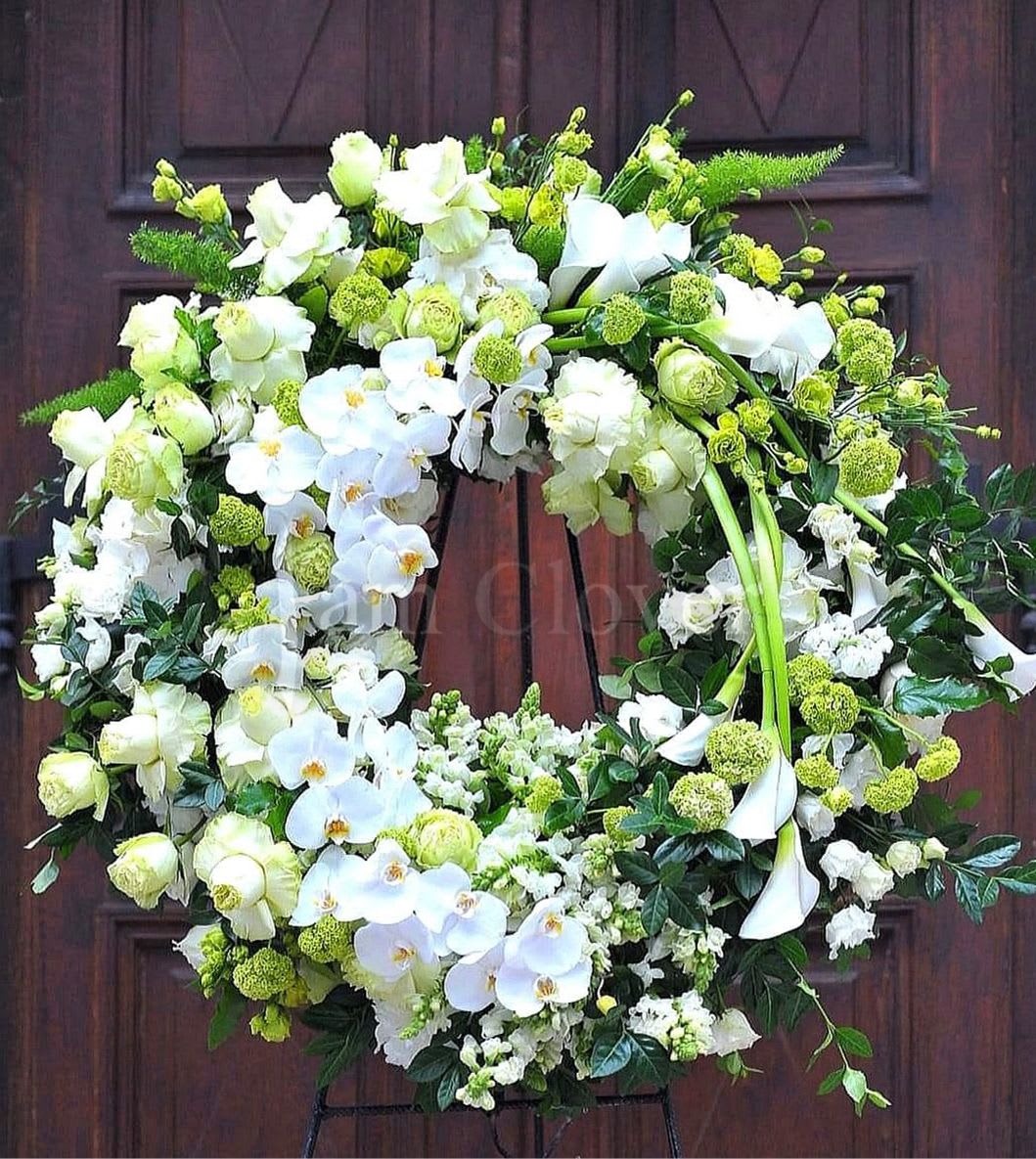 European Style White Wreath  - This design is a fitting and graceful farewell piece, honoring the loved one with a serene yet luxurious floral tribute.  For An elegant, European-style funeral wreath with a white color scheme, we use a mix of upscale, luxurious blooms that convey a sense of peace and grace. 	 Primary Flowers:    • White Roses: Classic and elegant, symbolize reverence and love.    • White Calla Lilies: Known for their sculptural beauty, represent purity, traditional for funerals.    • White Orchids: Elegant and sophisticated, add an upscale feel.    • White Hydrangeas: Provide fullness, softness, and a lush texture. Accent Flowers:    • White Ranunculus: Delicate and layered, add a soft texture.    • Lisianthus: Add a gentle and romantic look.    • Delphinium/Snapdragons: Add height and flow, European aesthetic. Greenery:    • Eucalyptus: Adds a soft green accent with a gentle fragrance.    • Italian Ruscus: Offers a delicate, draping look. 	 Fulfill your floral needs at I Am Clover in Ramona, CA, and experience the difference in quality, freshness, and care that comes with ordering locally.   Please ask about Delivery details.