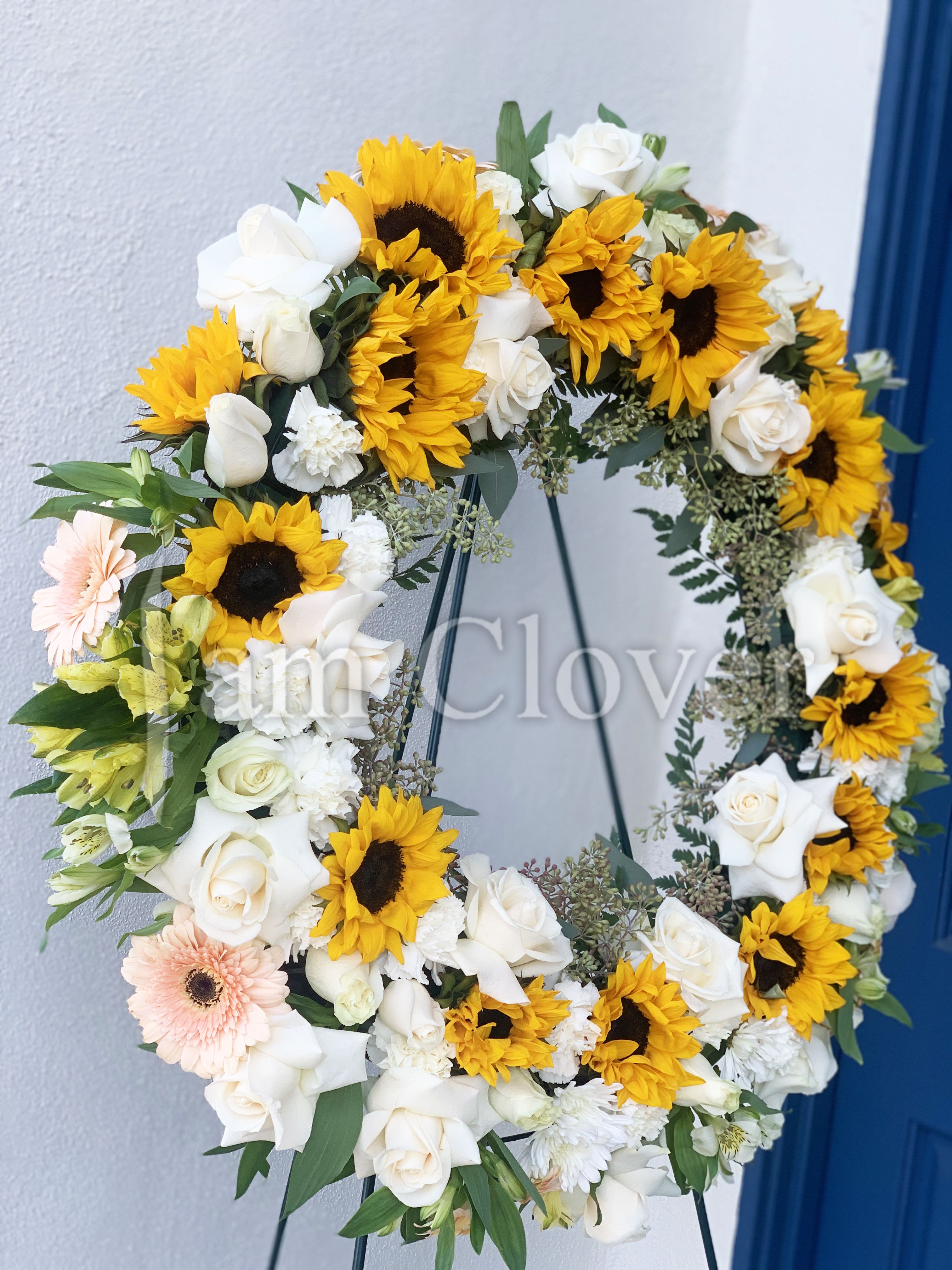 Sunflower and White Rose Wreath - This vibrant yet serene wreath symbolizes both the warmth of life and the purity of love. The combination of sunflowers and white roses evokes a sense of optimism, remembrance, and grace.  Fulfill your floral needs at I Am Clover in Ramona, CA, and experience the difference in quality, freshness, and care that comes with ordering locally.   Delivery: 2:30pm - 6:30pm Same Day Orders may take at least 6 hours to process and deliver Morning and Specific Delivery Time Requests:  will be charged a $15 convenience fee. Specific delivery times are acknowledged and we will do our best to accommodate, however we cannot guarantee on time delivery due to unforeseen events.  Gate Codes are mandatory for our delivery drivers to enter residential or commercial buildings. If you don’t know the gate code for a delivery, please contact the recipient and provide us with it or our driver can contact the recipient before beginning a delivery route to obtain the code. Our drivers will only wait five minutes outside the gate for a callback. If a driver has to leave a property, the delivery is reassigned for the next day and may charge an additional delivery fee. 