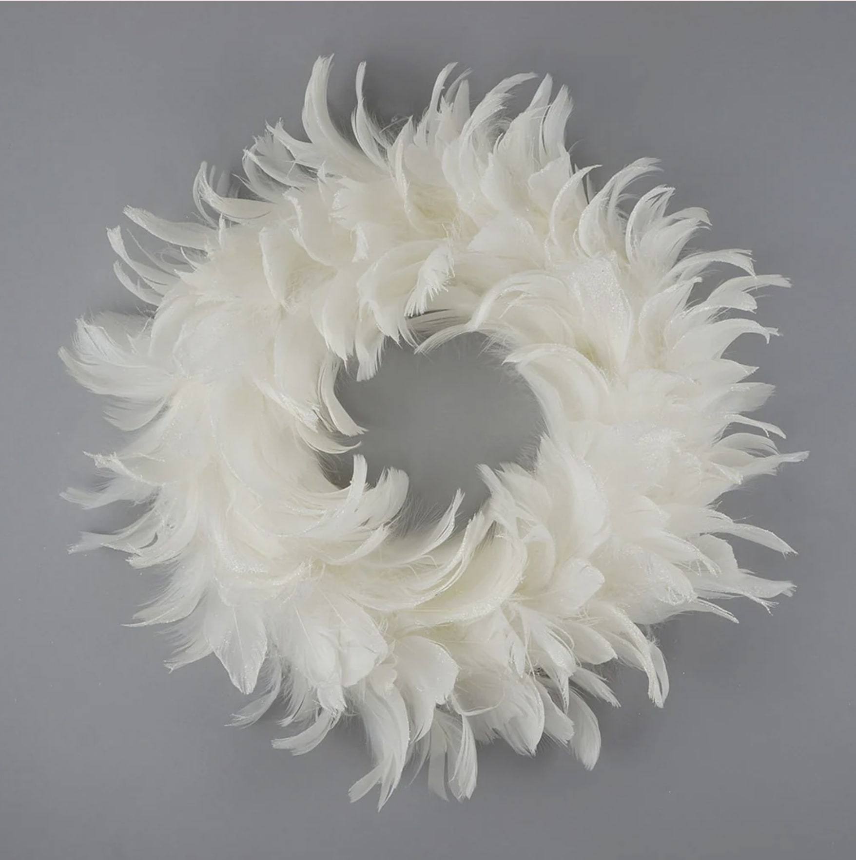 Handmade 12&quot; Goose Coquille Feather Wreath  - This handmade 12&quot; Goose Coquille Feather Wreath is a captivating piece that combines natural beauty with a touch of sparkle. Crafted from premium goose coquille feathers, the wreath features soft, delicate plumes arranged in a circular design that exudes elegance. The tips of the feathers are adorned with opalescent glitter details, adding a subtle shimmer that enhances the natural texture and shape of the feathers. The wreath's timeless charm makes it a perfect accent for any home, from seasonal décor to year-round displays, bringing a refined, artisanal touch to any space. Its handmade craftsmanship ensures that each wreath is a unique and exquisite work of art.