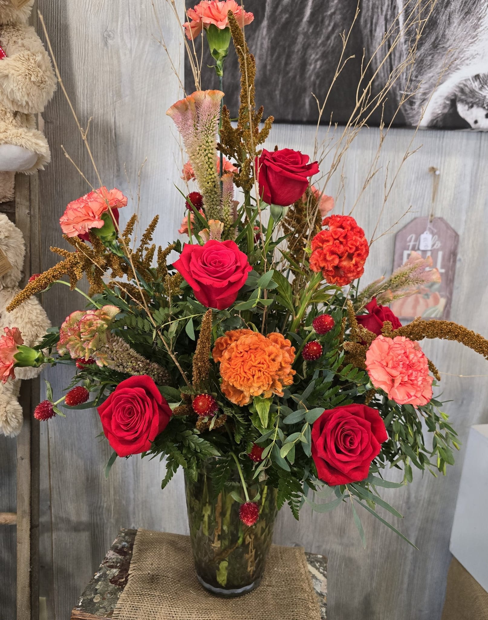 Sunset Passion Sunset Passion - A vase arrangement beautifully arranged with a ray of warm vibrant colors. Arranged with bold red roses, orange carnations, locally grown orange celosia and gomphrena. (Celosia and gomphrena flowers available during summertime only, similar substitutions made on off season)