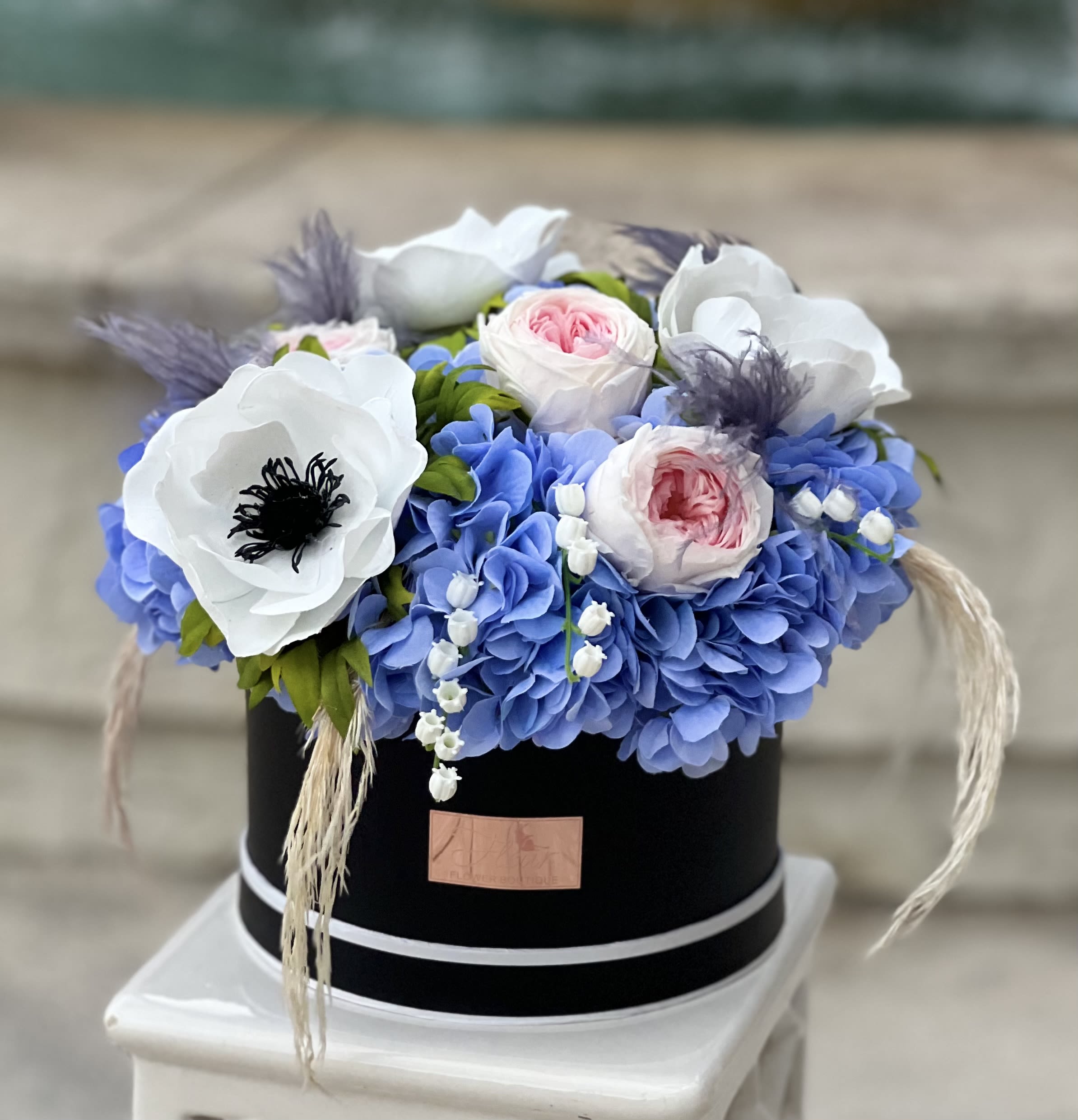 Celestial Bloom Grande - The Celestial Bloom Grande showcases a beautiful mix of blue hydrangeas, large white anemones, and pink and white garden roses, accented with dried elements. Presented in a sleek round black flower box with our signature gold logo, this large, luxurious arrangement offers a lasting, eco-friendly alternative to fresh flowers. Sustainable, low-maintenance, and full of elegance, it’s the perfect gift that brings timeless beauty and sophistication to any space.