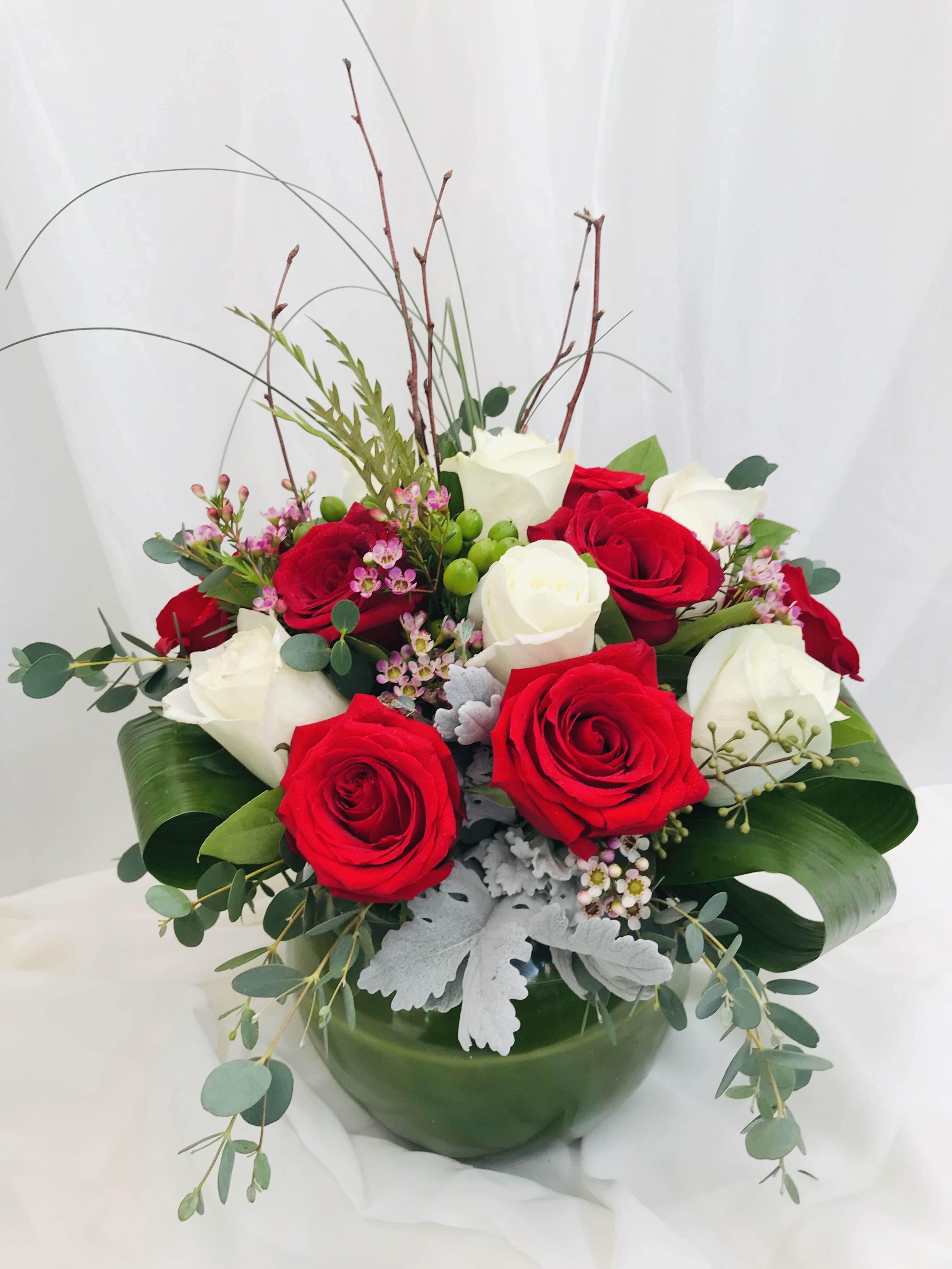Winter Love - This arrangmnet is made up of red and white roses and contains an assorted of greens including dusty miller and eucalyptus. The elegant arrangmnet sits in a crystal bowl with a leaf wrapping around the inside to conceal the stems. 