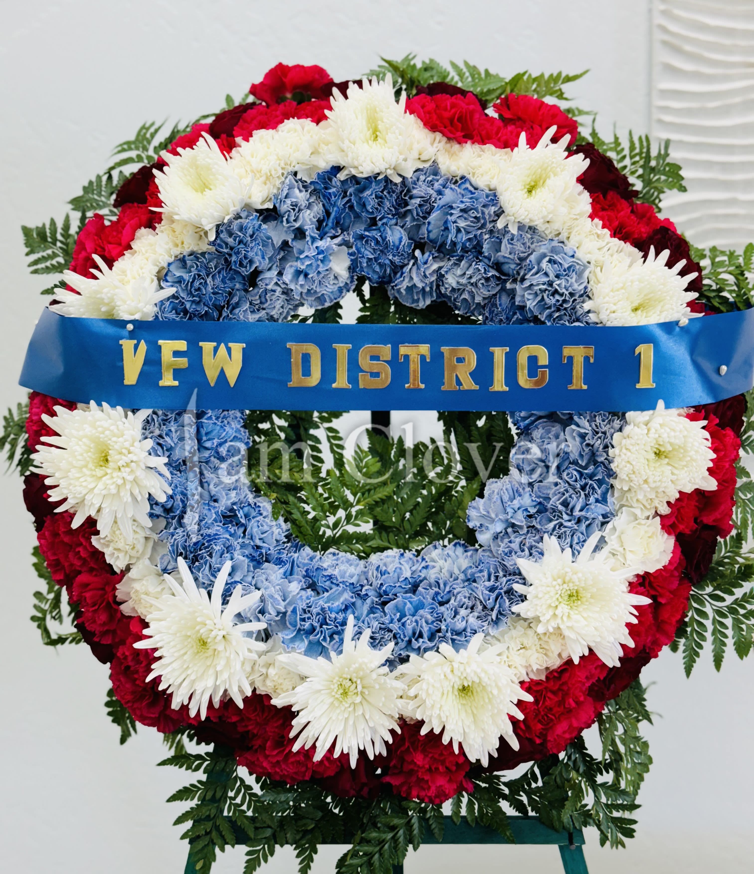 Red, Blue and White Wreath  - Patriotic Standing Wreath A tasteful and elegant funeral arrangement that honors your loved one with a blend of red, blue, and white flowers, symbolizing strength, loyalty, and peace. Displayed on a sturdy easel, this standing wreath is a beautiful tribute for memorial services or graveside ceremonies. Available in three sizes to accommodate your needs: 	•	18 inches – For a subtle yet meaningful tribute. 	•	22 inches – A balanced, classic display. 	•	26 inches – For a larger, prominent expression  Fulfill your floral needs at I Am Clover in Ramona, CA, and experience the difference in quality, freshness, and care that comes with ordering locally.   Please ask about Delivery details.
