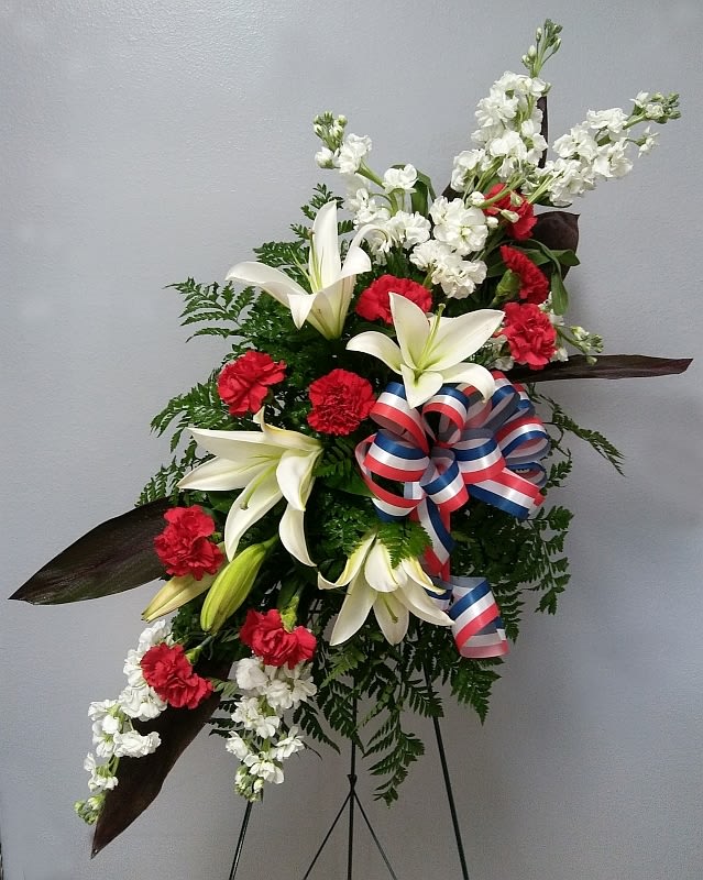 Stars of Life Standing Spray - This standing spray is made with white stock, white oriental lilies, red carnations, and a red, white and blue bow.