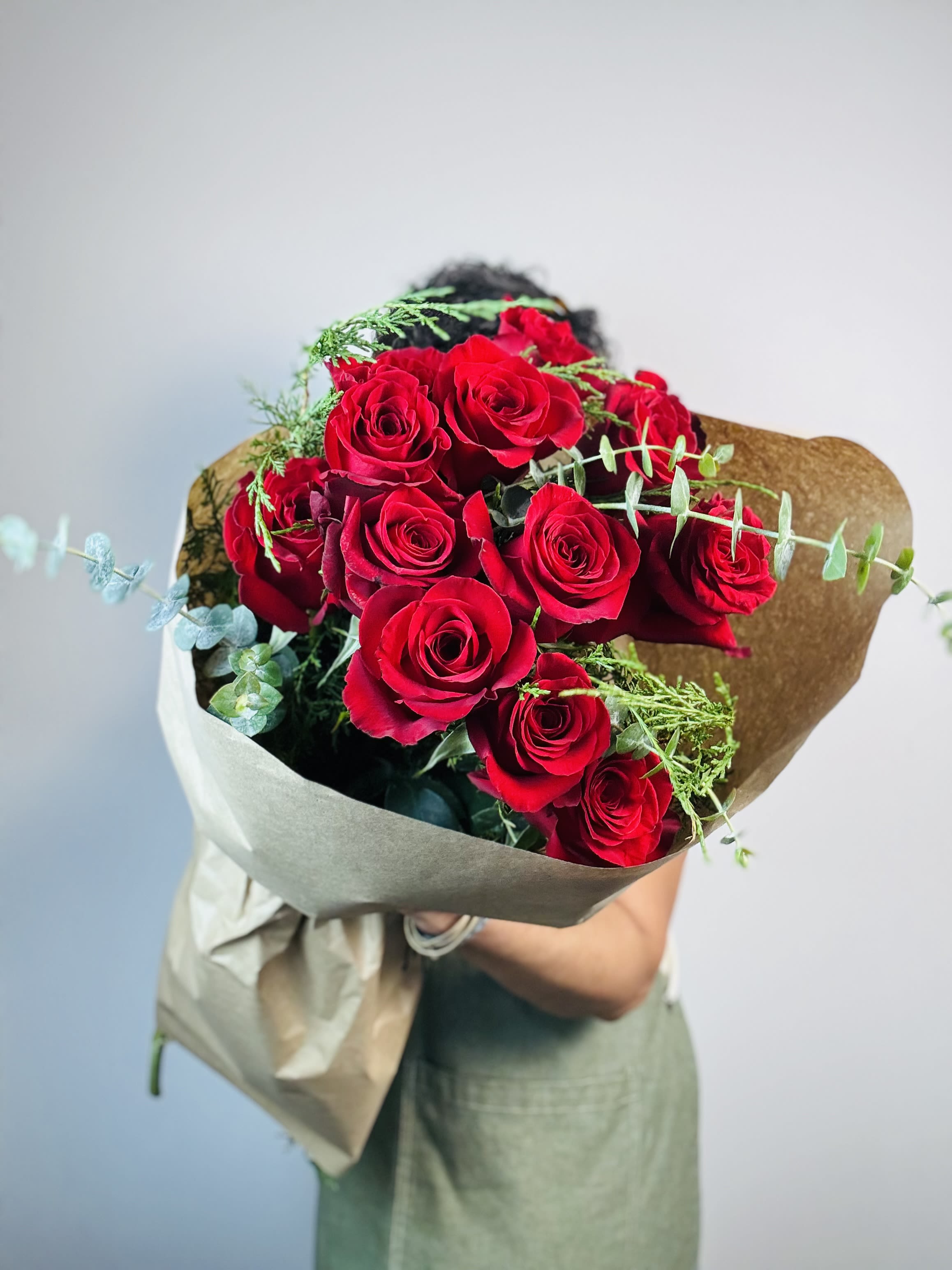 One Dozen Red Roses and Greenery - Hand Tied - Celebrate the holidays with a relaxed, hand-tied bouquet featuring stunning Freedom roses, known for their rich, deep red color and soft, velvety petals. Paired with fresh winter greenery, this effortless design brings a touch of festive elegance to any occasion.   Perfect for gifting or decorating your home, this easy, grab-and-go bouquet is available every day throughout the holiday season, offering the perfect blend of beauty and seasonal cheer.