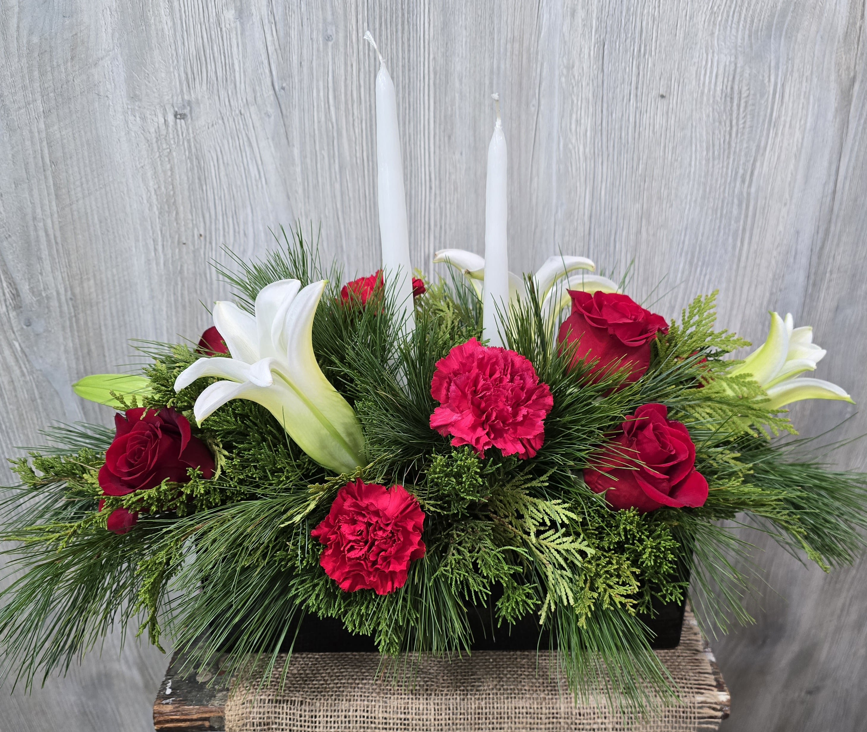 Light of Chirstmas  - A beautiful elegant centerpiece with candles, full of fresh pine, lilies, roses, and carnations!  Deluxe and premium pricing includes more flowers! Container may vary with same elongated style. 