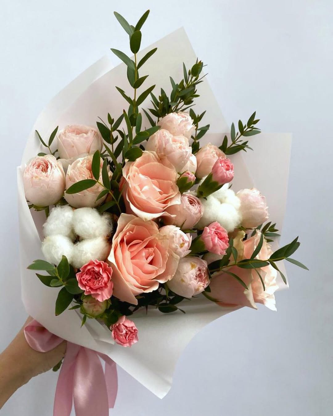 Delicate Cotton &amp; Roses - This bouquet is a tender composition of soft peach and blush pink roses, delicate spray carnations, and unique cotton flowers, beautifully complemented by lush greenery. The arrangement is wrapped in elegant white paper and tied with a satin pink ribbon, adding to its romantic charm.