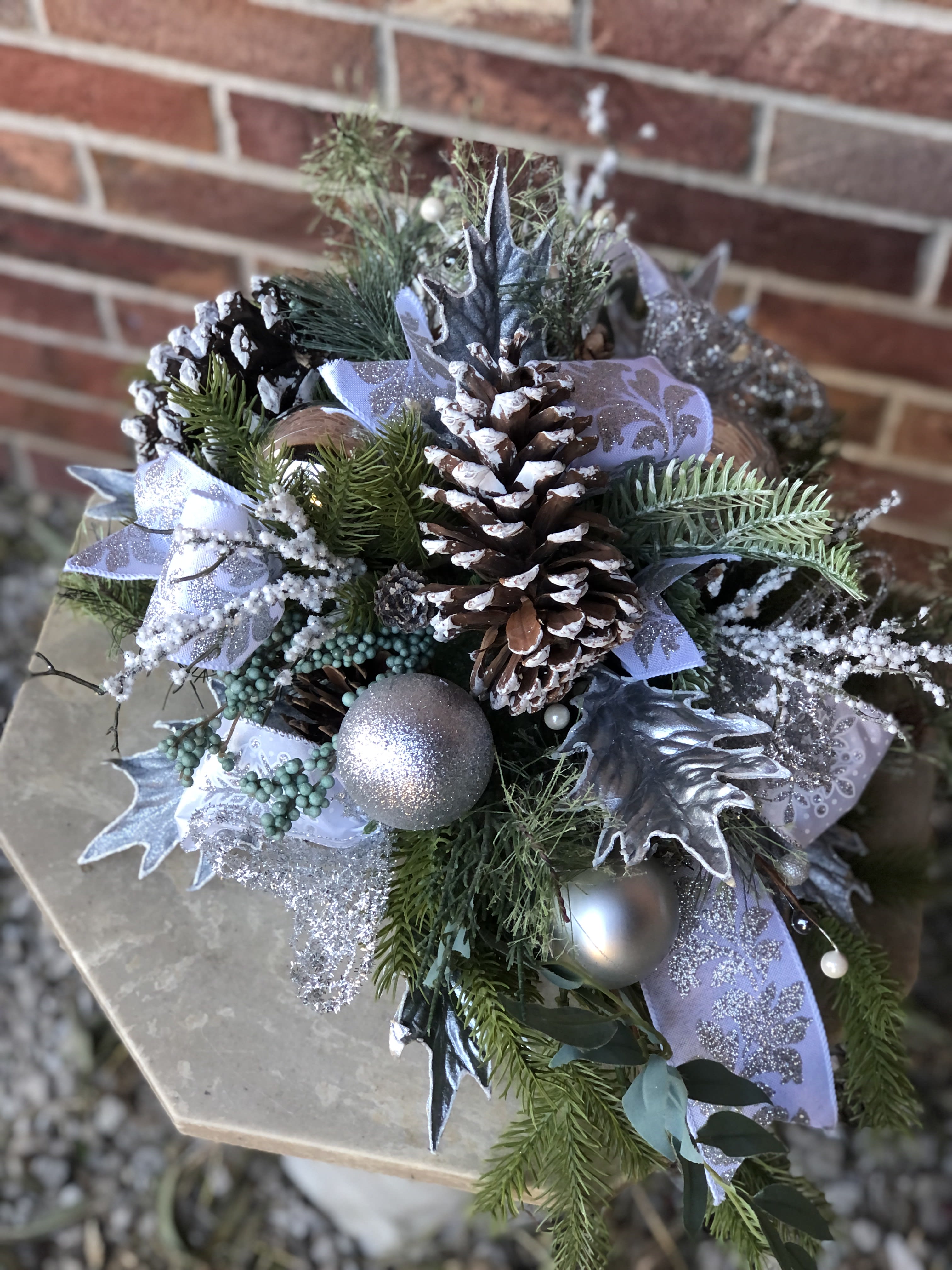 Silver Snow Christmas Centerpeice Silver Snow Christmas Centerpeice - Frosted pinecones, silver leaves and ribbon, and shiny ornaments make this a sparkly piece for your holiday decor! Approx. 18" x 12"