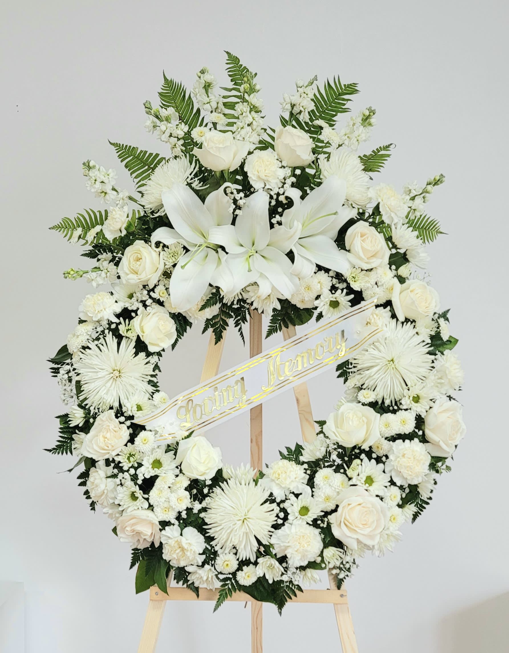 White Wreath With Top Spray - A beautiful mix of white roses, carnations, lilies plus other white filler flowers on a wreath with a top spray. Measures approximately  3ft tall x 28&quot; wide on a 5ft tall easel. Loving Memory Banner included. For a custom banner, please add by searching &quot;Sympathy Banner&quot;.