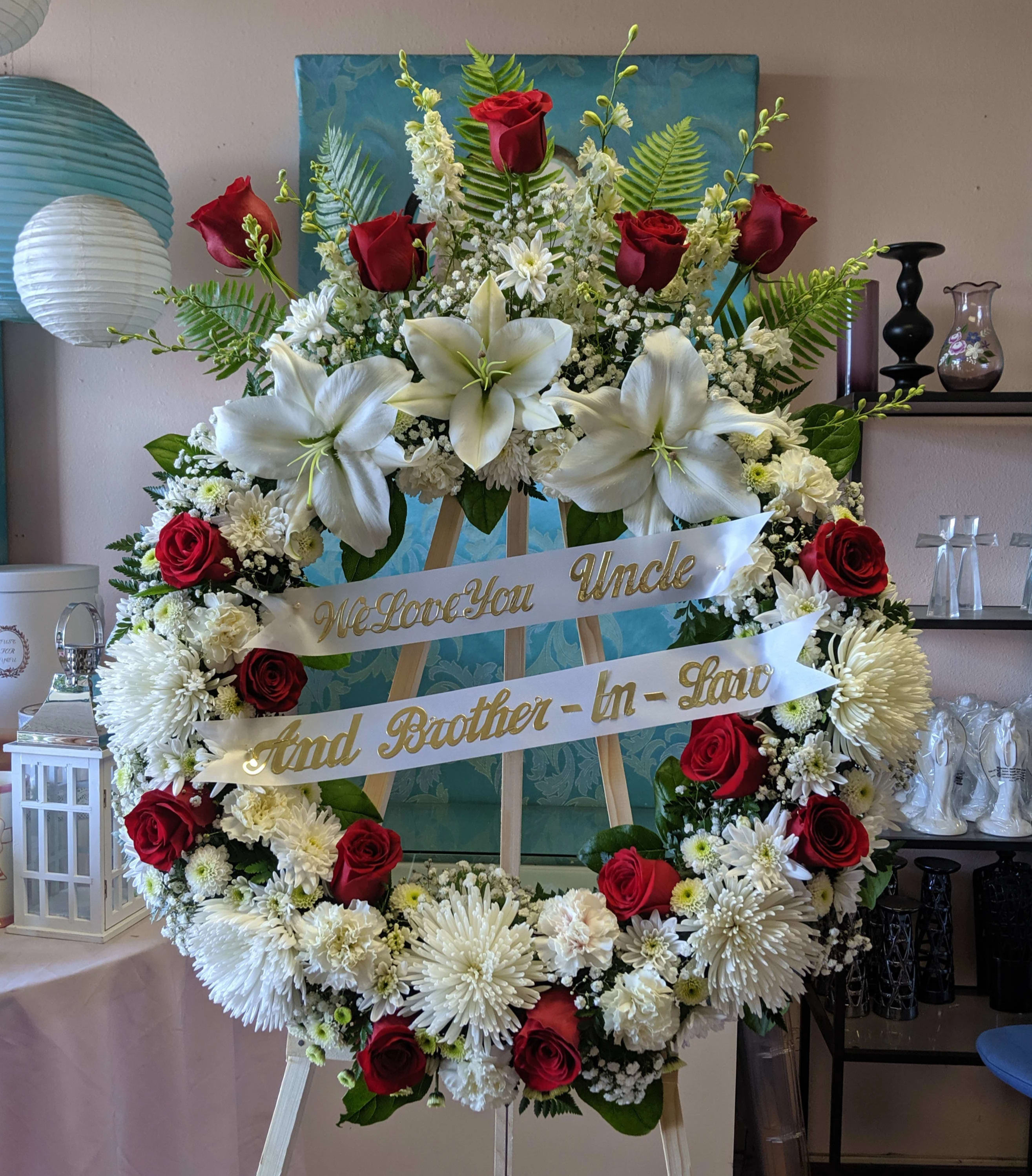 Red Rose Wreath Top Spray Red Rose Wreath Top Spray - This medium size wreath comes with 16 red roses, mums, carnations, and a top spray with lilies and larkspur plus other filler flowers. It is absolutely beautiful. Upgrades available. For a custom banner, please add by searching "Sympathy Banner".