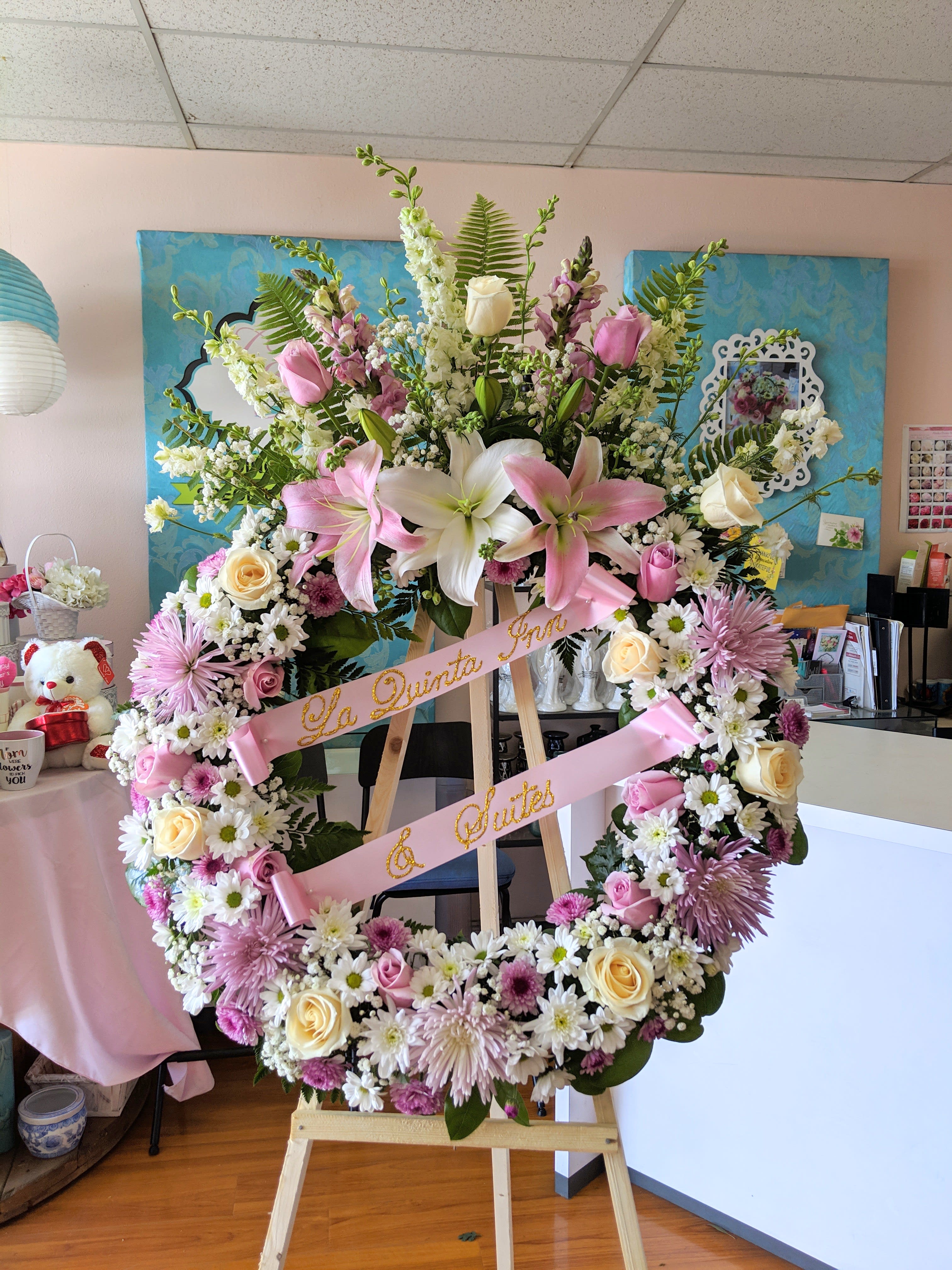 Pink Wreath With Top Spray - Large wreath with a top spray in a mix of pinks, lilac, white roses, lilies, and several other beautiful blooms. For a custom banner, please add by searching &quot;Sympathy Banner&quot;.