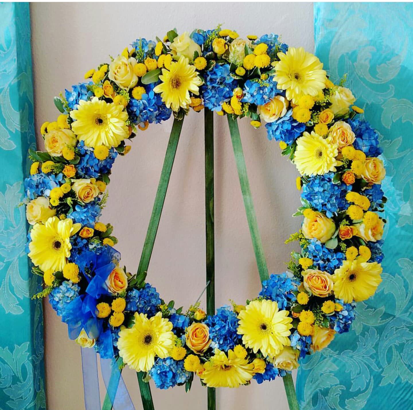 Spirit In The Sky Wreath - This wreath is a great expression of the beautiful blue sky and its vibrant yellow sun rays. Yellow gerberas and roses with blue hydrangea are this wreath's perfect combination. For a custom banner, please add by searching &quot;Sympathy Banner&quot;.