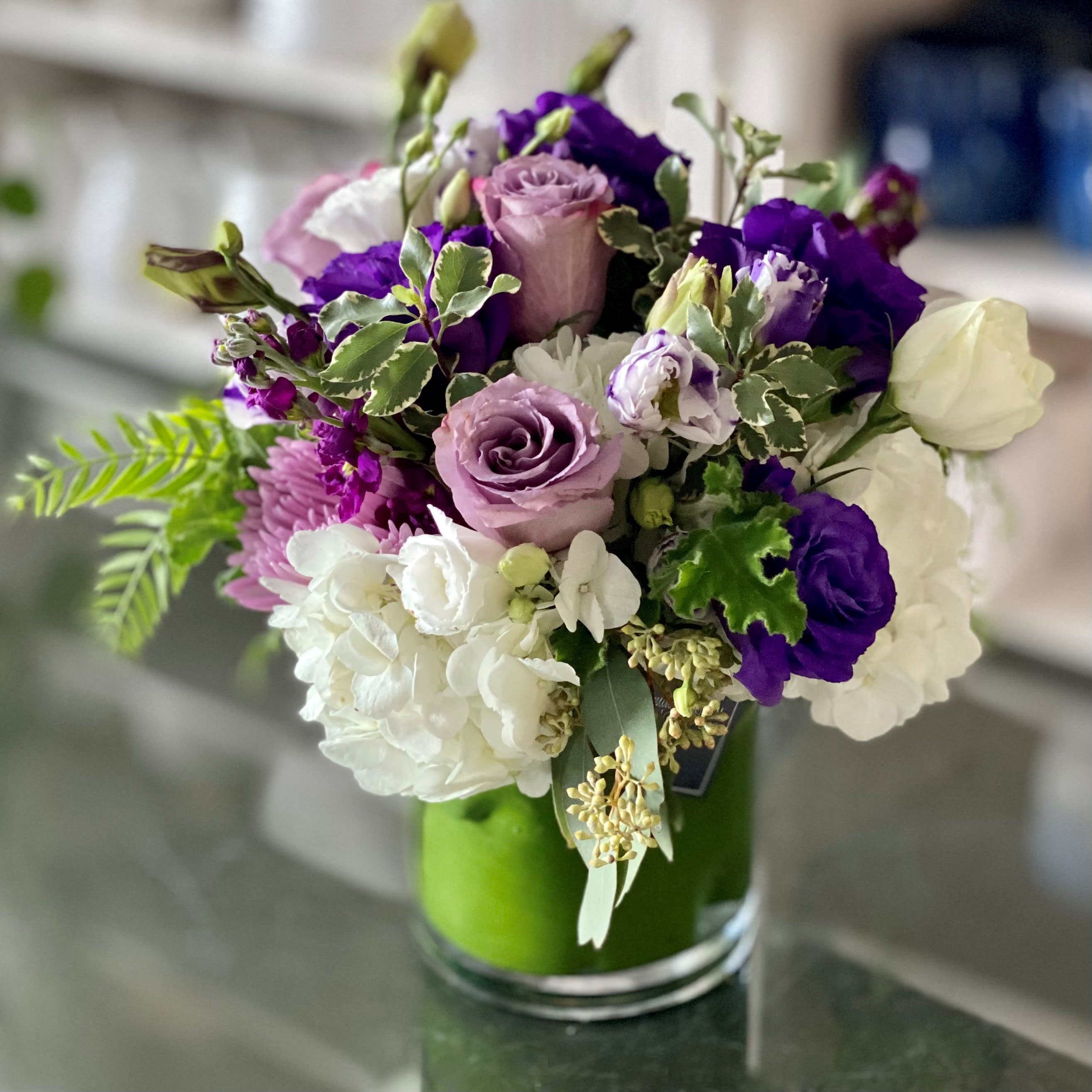 Descanso Descanso - Say hello to your very own piece of paradise with our Descanso arrangement. With its captivating combination of vibrant Lavender Roses, White Spray Roses, Purple Lisianthus, and other assorted blooms in a classic 5x6 clear cylinder vase, it’s sure to bring joy to family and friends of all ages. And adding the perfect touch of contrast is a simple sprig of seeded Eucalyptus – creating an even more delightful display! So whether you want to surprise someone special or brighten up your own space, Descanso is definitely your new go-to! Don’t wait; add some paradise to your home today.