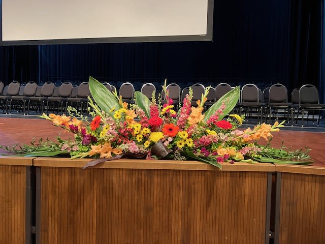 Stage flowers - This bouquet could adorn any stage beautifully.  This event actually had three of these beautiful and colorful bouquets adorning the stage.  These bouquets include gerberas, gladiolus, larkspur, daisy mums, accompanied by large leaves, among others as available.  