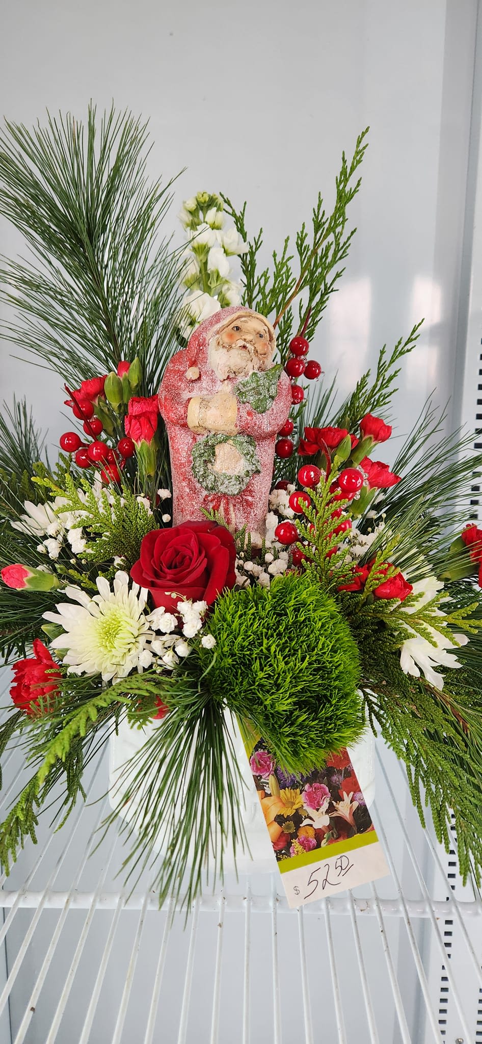 Santa Season Santa Season - This Santa is surrounded by mixed evergreens and traditional red and green flowers.