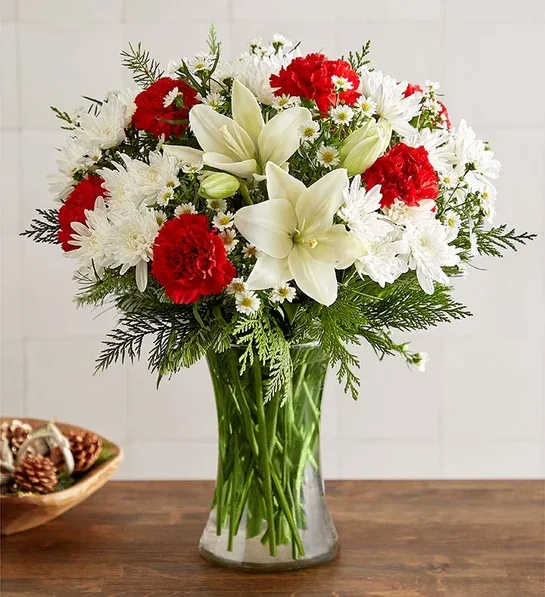 holiday charm holiday charm - All-around arrangement with red carnations, white Asiatic lilies, cushion poms, and monte casino; accented with assorted Christmas greenery