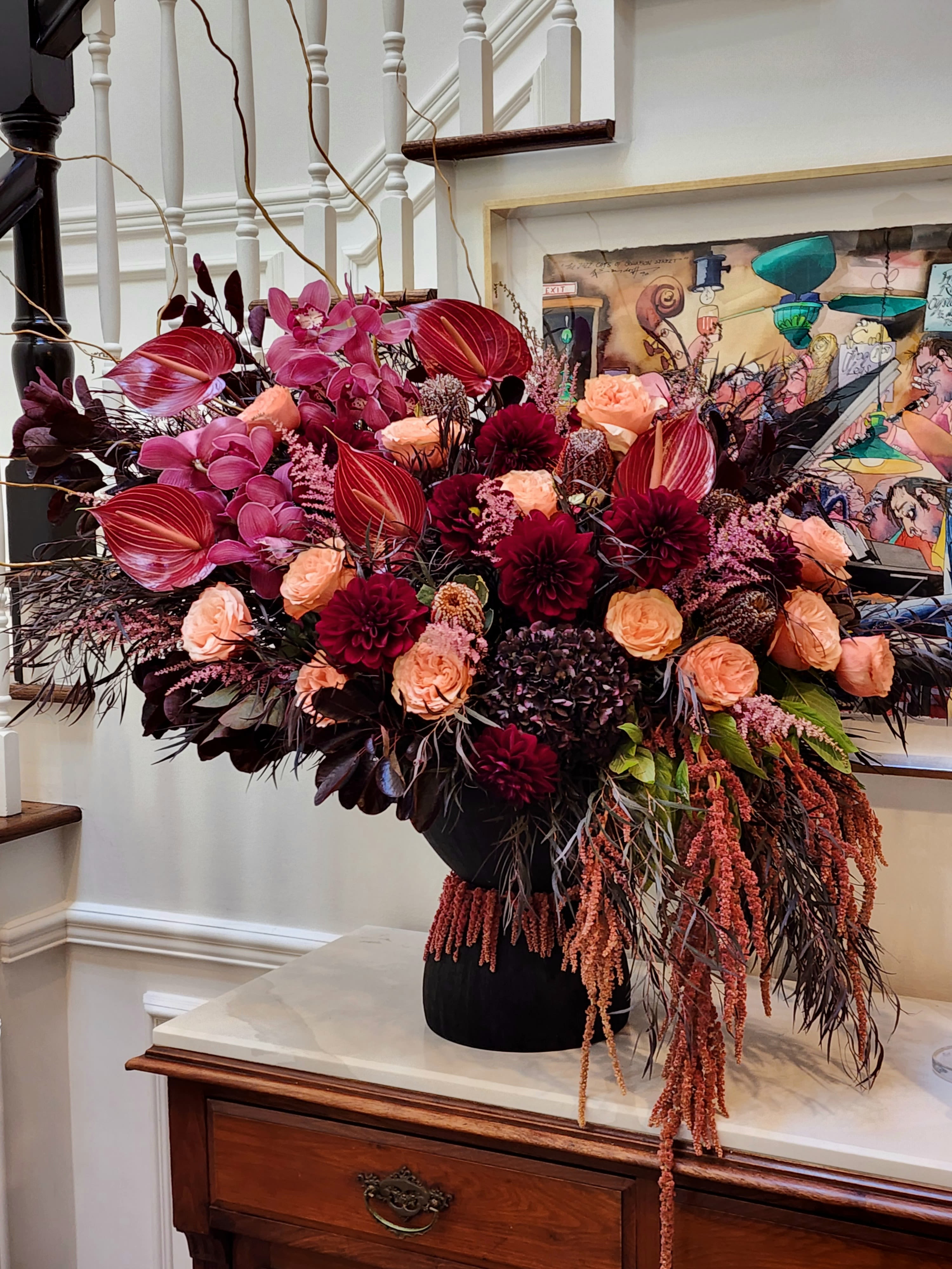 Sophistication -  This stunning arrangement features deep burgundy dahlias, peach roses, and exotic pink anthuriums complemented by orchids and textured foliage for a dramatic, luxurious effect. Cascading amaranthus adds movement and elegance, making it a perfect centerpiece for upscale events or grand home decor