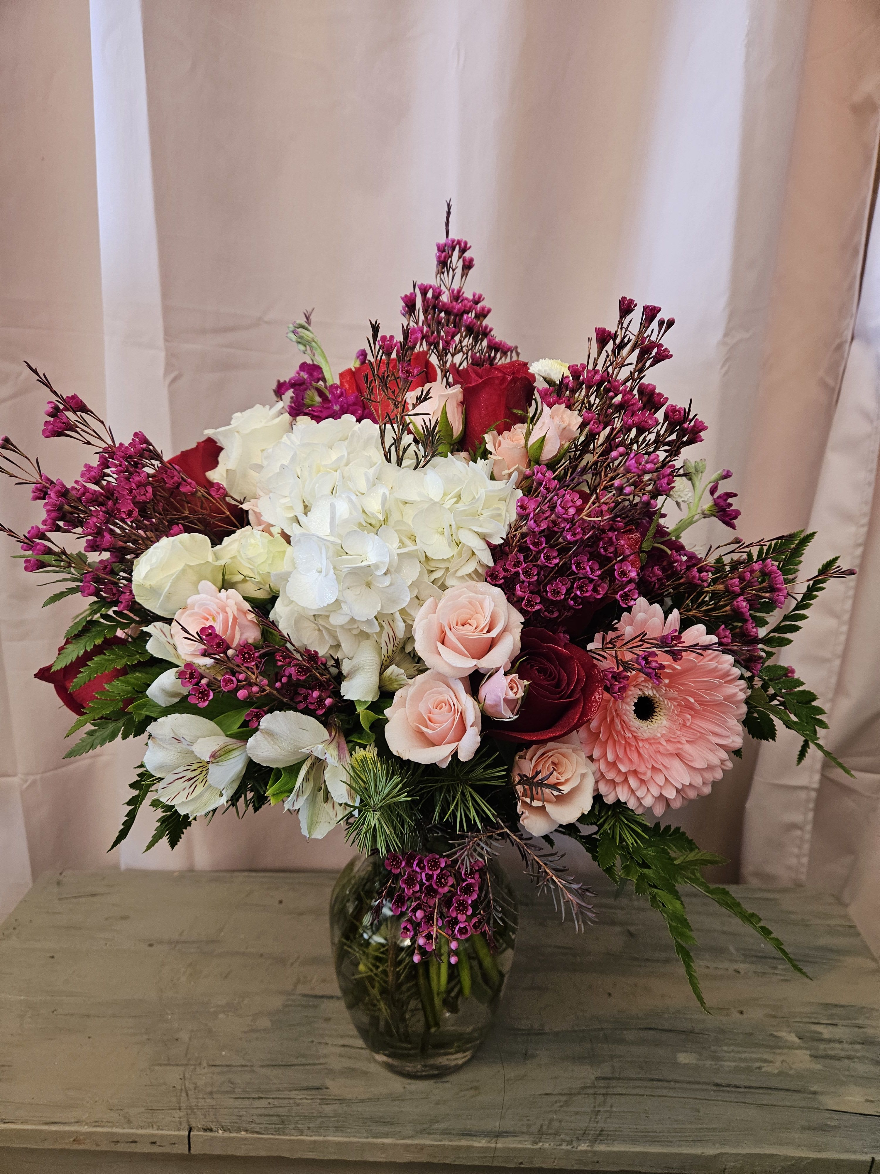 The Roxanne - Bright and colorful vase arrangement filled with red and white roses, pink spray roses, white hydrangea, purple stock, and pink gerber daisies.