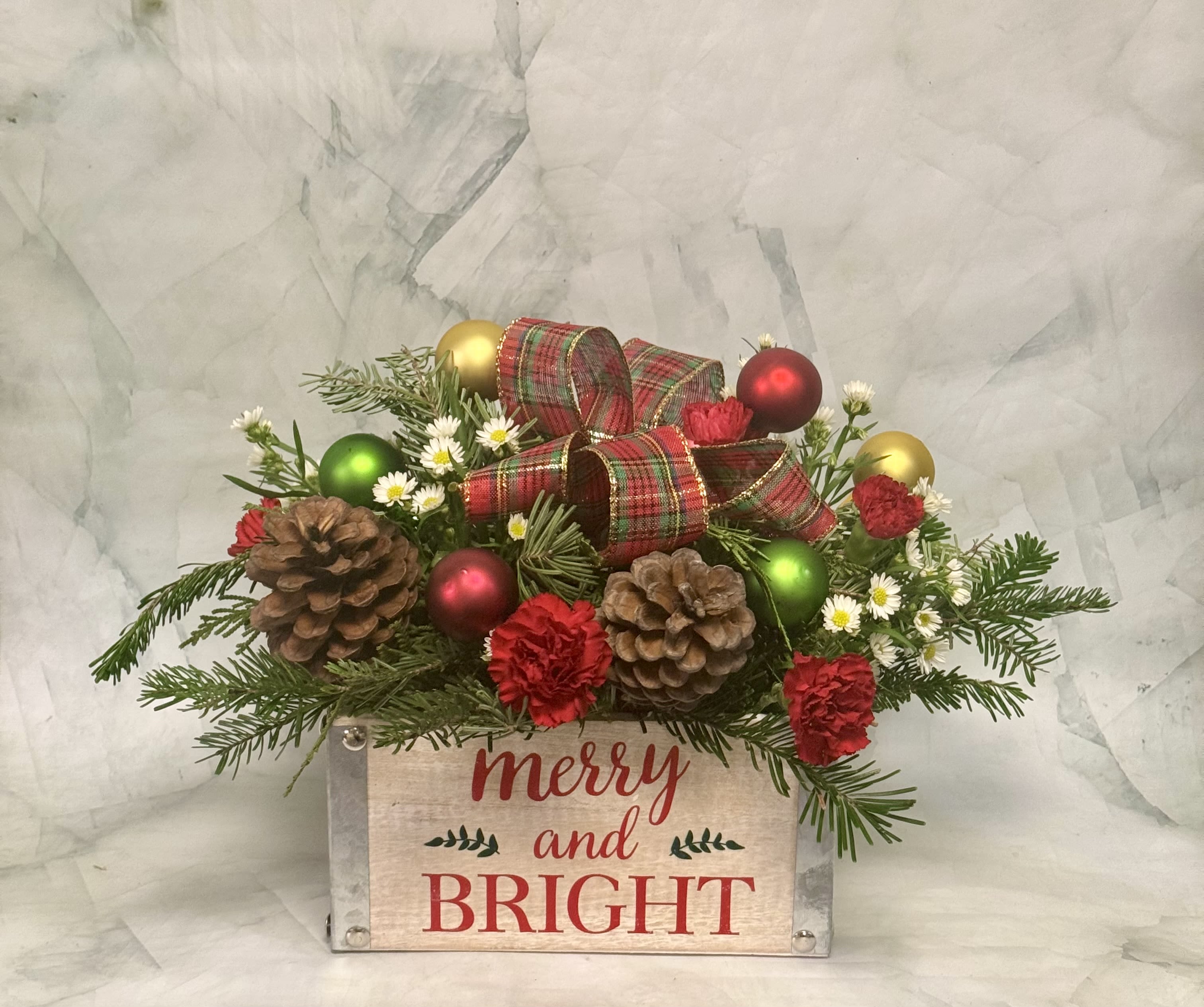 Merry and Bright  - This arrangement has it all! It certainly is merry and bright! This one of a kind arrangement is uniquely designed in a wooden box that can be repurposed as a beautiful decoration. The arrangement is simple as it only includes Christmas greens, pinecones, aster, a bow, and Christmas ornaments. This is a long lasting arrangement which makes it perfect for lasting for the entire holiday season. 
