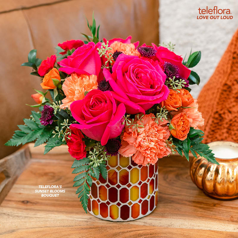 Teleflora's Sunset Blooms Bouquet Teleflora's Sunset Blooms Bouquet - As mesmerizing as a summer sunset, this majestic mix of colorful roses in a magnificent mosaic glass vase is a gift they'll treasure. This arrangement includes hot pink roses, orange spray roses, orange carnations, purple button spray chrysanthemums, miniature hot pink carnations, seeded eucalyptus, leatherleaf fern and huckleberry. Delivered in Teleflora's Autumn Radiance Mosaic vase.