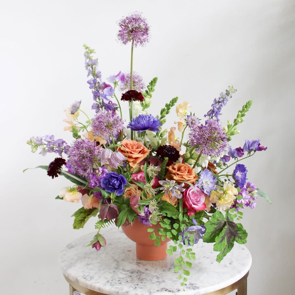 Alliums wild flowers  - Bring Timeless Elegance to Your Space”  Introducing the “Whispering Garden Arrangement”—a stunning medley of nature’s finest blooms. This enchanting display features: 	•	Majestic Alliums with their globe-shaped blossoms, exuding sophistication and grace. 	•	Lush orange roses, the timeless symbol of warmth and energy. 	•	Soft, cascading greens and delicate wildflowers in shades of violet, blush pink, and cream for a harmonious balance of color and texture.  Perfect for celebrations, gifting, or brightening up your home, this hand-crafted masterpiece turns any space into a garden oasis.  Order now and bring the beauty of a blooming meadow to your doorstep!