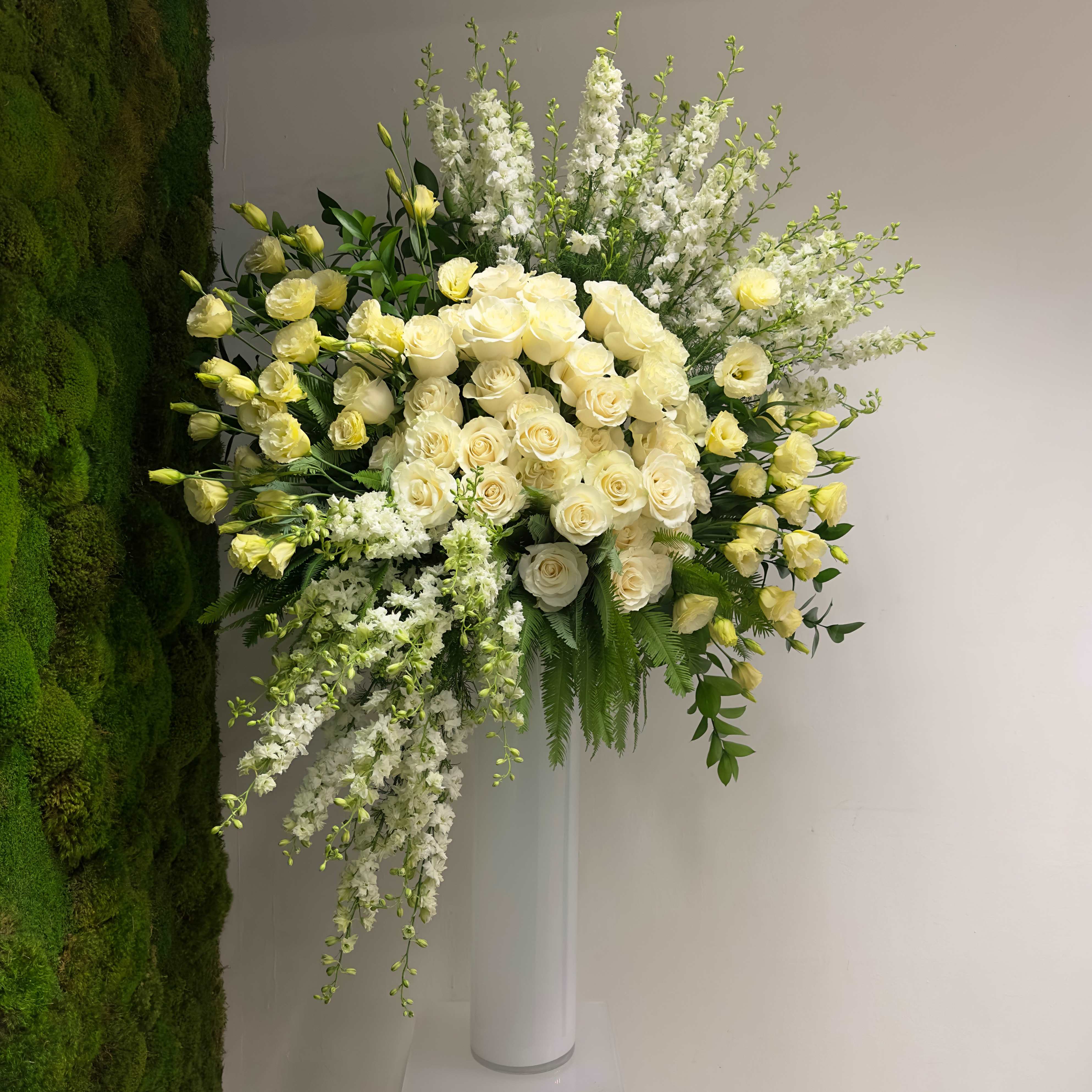 Snowfall Snowfall - A masterpiece that exudes magnificence from every angle. Standing tall at 5 feet, including its glass slick vase, this arrangement embodies sheer elegance with its luxurious display of white roses, lisianthus, and larkspur meticulously arranged to perfection. Dimensions: Approximately 36" (H) x 30" (W)