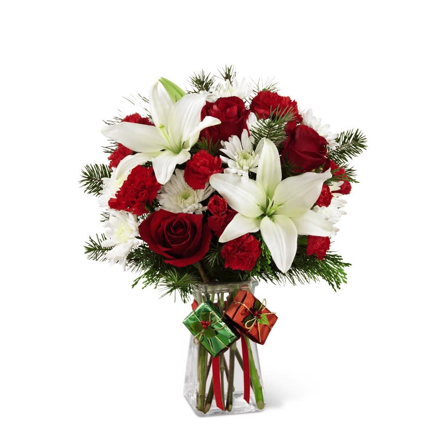 The FTD Joyous Holiday Bouquet - Rich red roses, carnations, and mini carnations are brought together with brilliant white Asiatic lilies and chrysanthemums accented with lush holiday greens to create an incredible fresh flower arrangement. Presented in a clear glass gathered square vase embellished with red ribbon at the neck dangling foil-wrapped present accents to give it a festive look, this holiday flower bouquet will make an excellent Christmas gift for your favorite friends, family or co-workers.