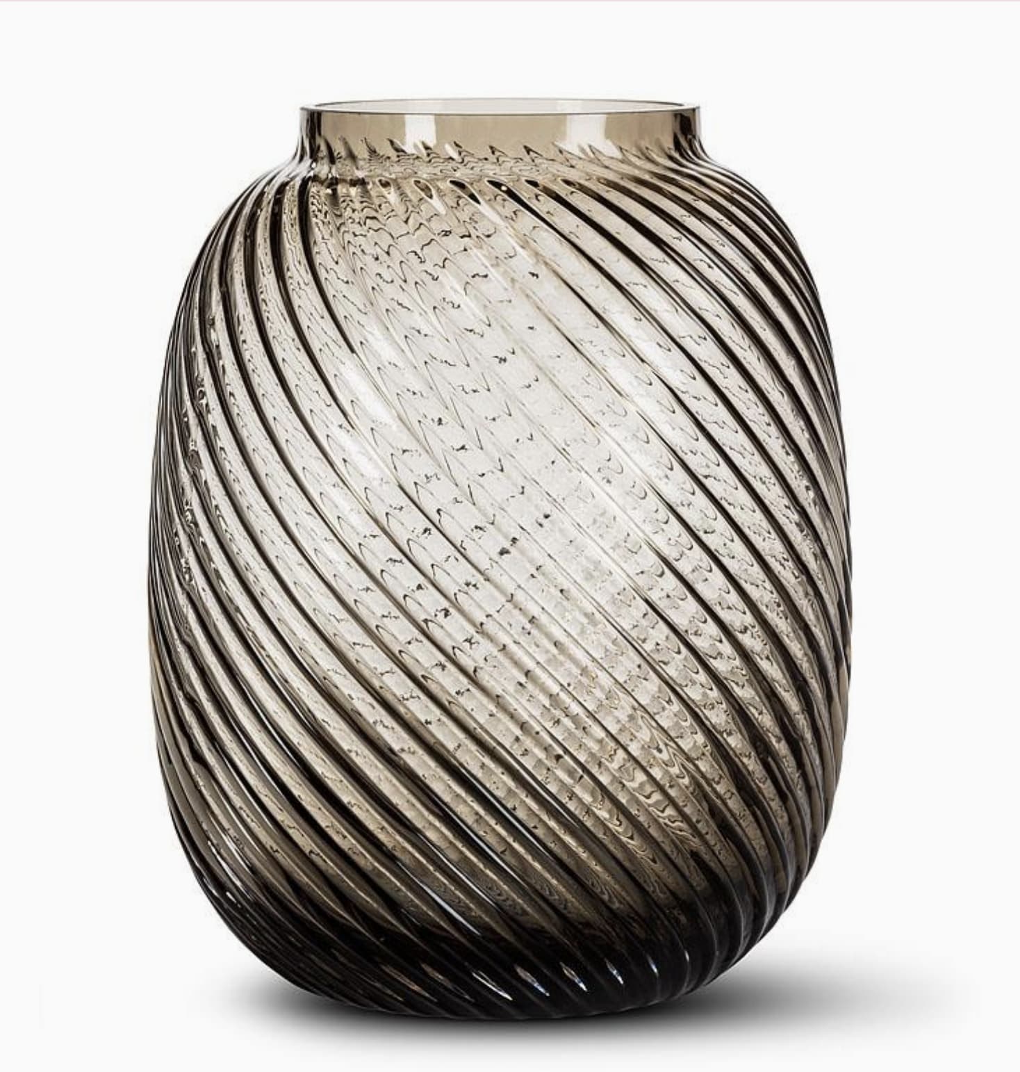 Medium Swirl Barrel Vase - Grey - The Medium Swirl Barrel Vase is a striking choice for those looking to enhance their decor with a piece that complements both floral and candle arrangements. Crafted from grey tinted glass, this vase features a simple cylindrical shape, beautifully accented with a diagonal textured ribbed pattern. This unique design not only adds visual interest but also captures and reflects candlelight to heighten the mood and atmosphere in any setting. Measuring 7.3 x 7.5 x 9.5 inches, it’s perfectly proportioned for use on any table, shelf, or mantel. Ideal for creating a sophisticated and inviting space, this vase is available at Chartreuse by Roje.