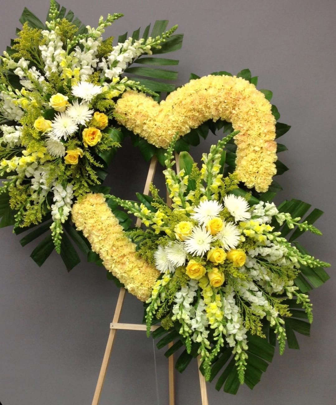Golden Grace Heart Golden Grace Heart - Set on a sturdy easel, this wreath is accented with lush greenery and delicate filler flowers to enhance its beauty and elegance. Its radiant design conveys heartfelt condolences and serves as a comforting tribute at any funeral or memorial service. Perfect for honoring the memory of a cherished loved one, this wreath expresses warmth, compassion, and everlasting love.