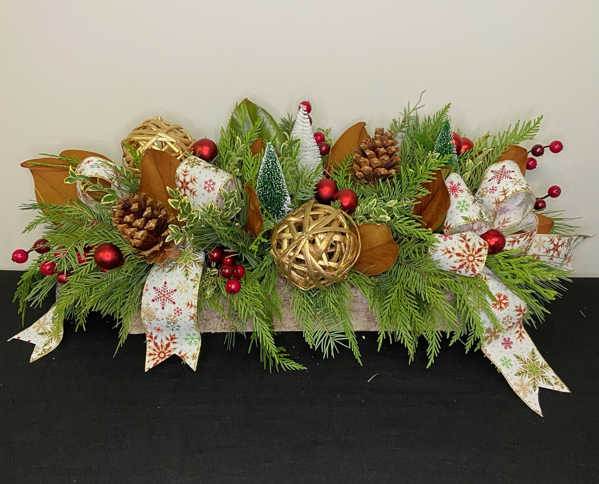Winter Wonderland by Chasing Petals - A long and low arrangement of mixed evergreen, accented with deep red berries, gold vineballs, and pinecones. Without any fresh flowers this will last for weeks with just regular watering! Perfect for the hostess who's hosting gatherings all month long!   Please note, ribbon and bobble colours are adjustable, please call us with any inquiries.