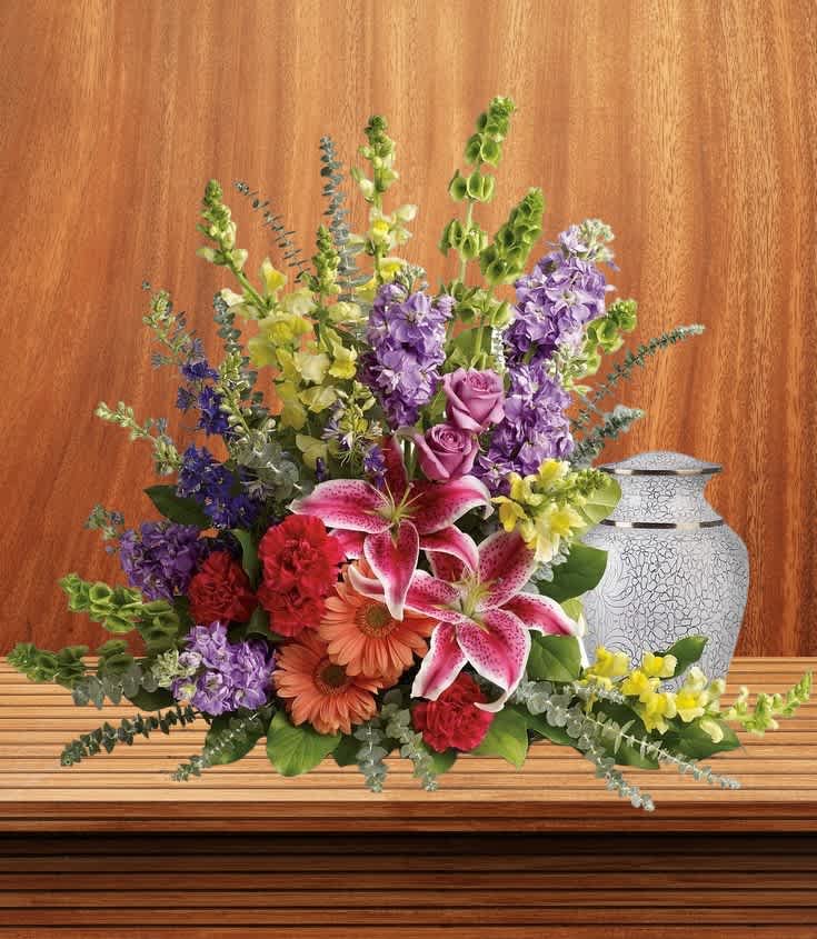 Shades of Feith - Radiate warmth and elegance with our urn arrangement adorned in vibrant orange, red, and lavender flowers, accented with stunning stargazer lilies. This beautiful display offers a heartfelt tribute, celebrating cherished memories and honoring a life with grace and beauty. Approximately  25w x 29H