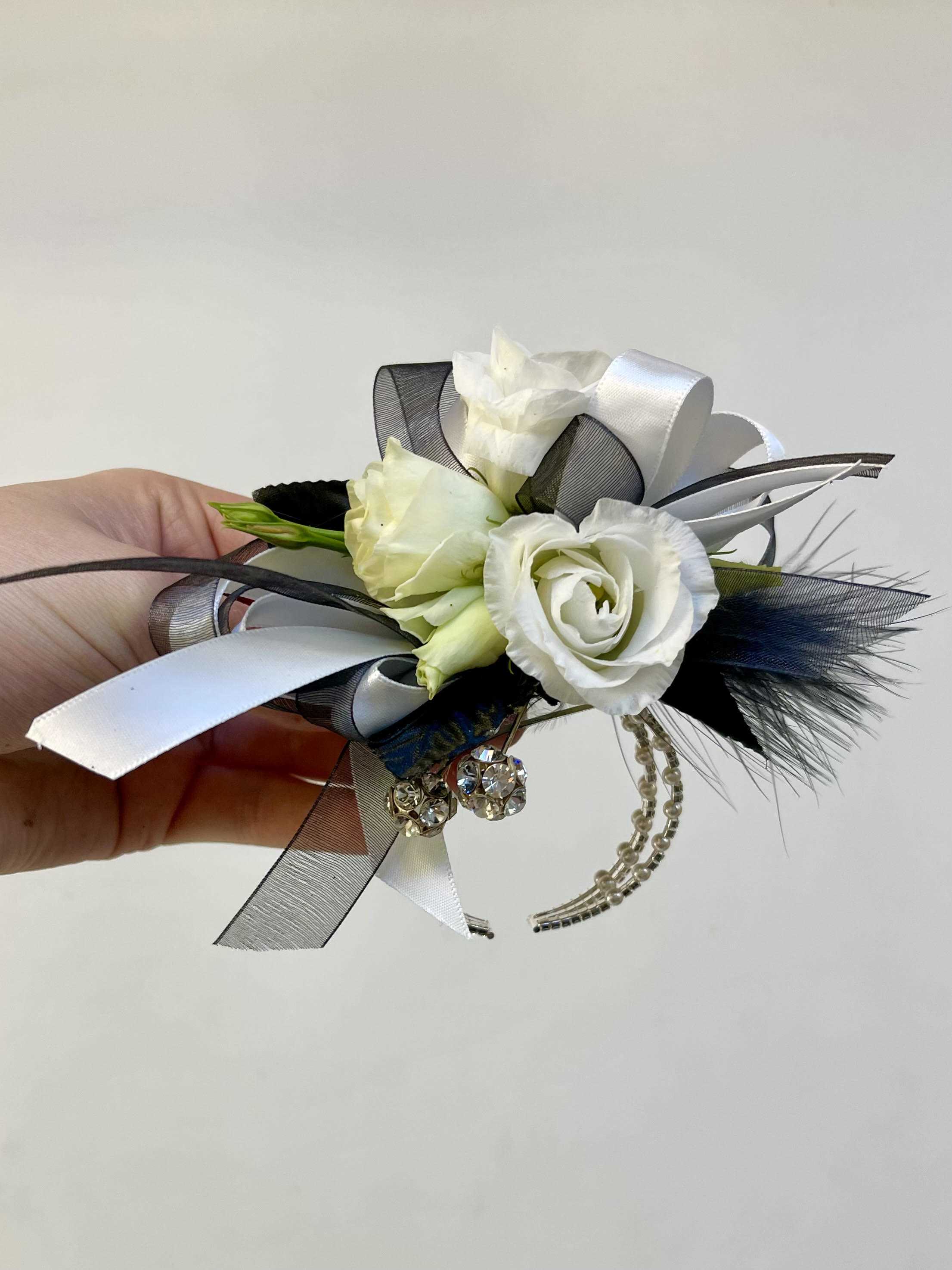 White and Black Wrist Corsage  - Elegant white roses wrist corsage with black accents including ribbon gems and feathers on a lovely keepsake silver band.  Corsages are sold by size Small (50) Medium 888 our most popular size (60) or Large (70).  personalize your corsage by choosing specific color, accents, size and band.