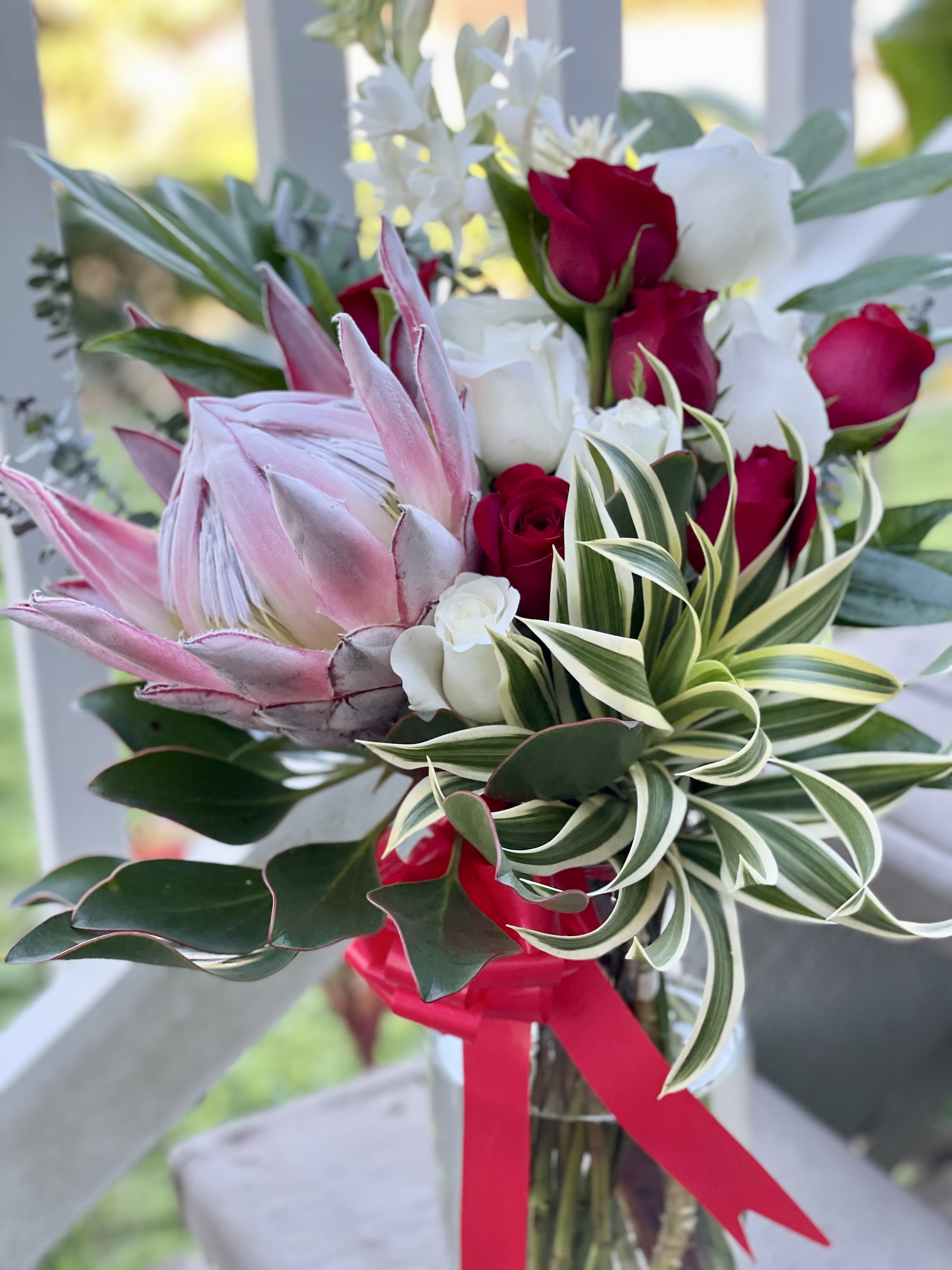 Pua Kealoha - Blossom of Love Pua Kealoha - Blossom of Love - A delicate harmony of Maui-grown king protea and romantic red roses, Hinahina Pua radiates feminine beauty and grace. A perfect gift to celebrate love and cherished moments.