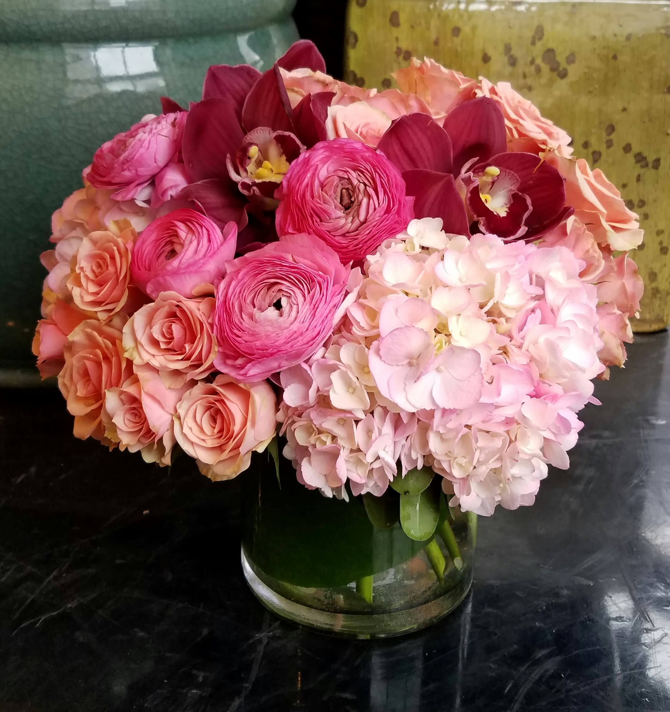 Funny Face Funny Face - Our ode to Audrey Hepburn, the sweet arrangement features blush pink Hydrangea, multi-petaled Ranunculus, champagne hued Spray Roses and mauve Cymbidium Orchids with complementary blooms in a leaf wrapped glass cylinder.